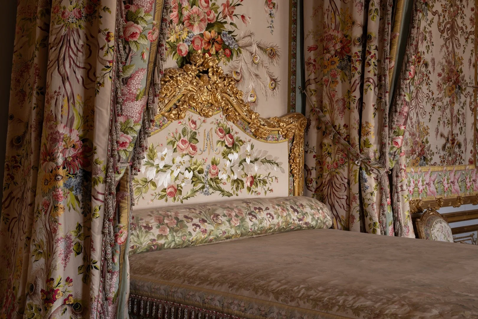 Opulent bedroom with floral and gold decorative bed frame, matching floral curtains, and embroidered wallpaper.