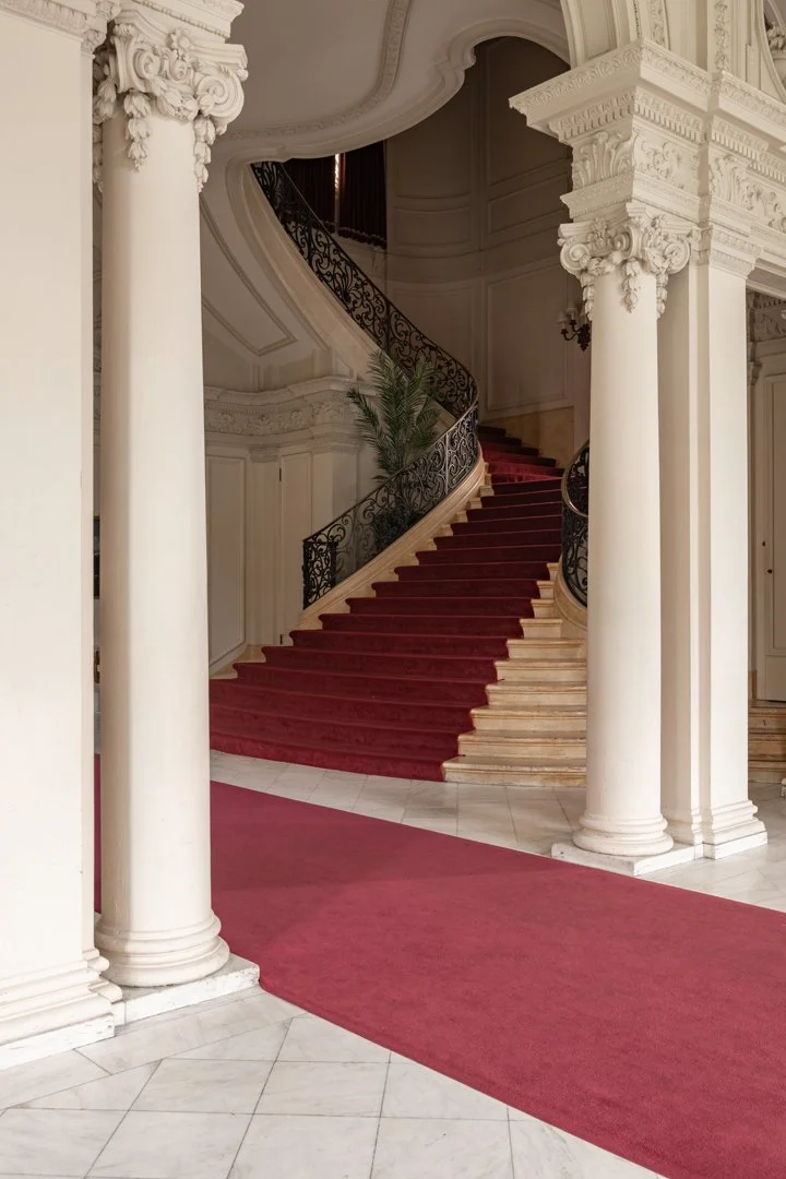 Grand staircase with red carpet and ornate white columns in an elegant interior.
