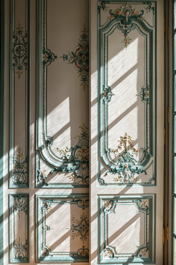 Decorative vintage wooden door with ornate carvings and floral motifs, illuminated by sunlight casting striped shadows.