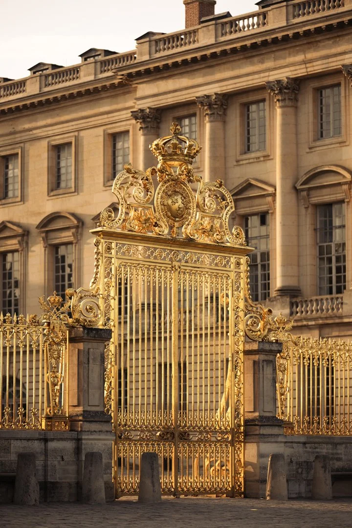 A gold ornate gate in front of a large historic stone building with multiple windows.