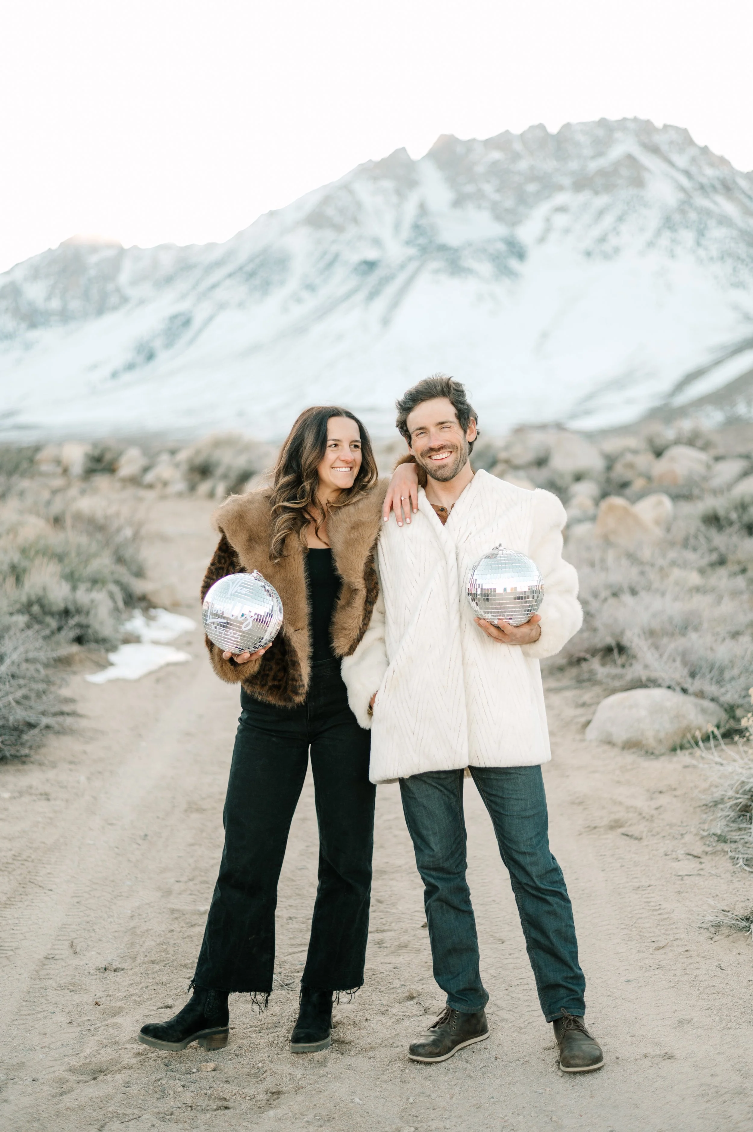 Bishop engagement photos of a good looking couple in front of snow capped sierra nevada mountains holding disco balls wearing fur coats
