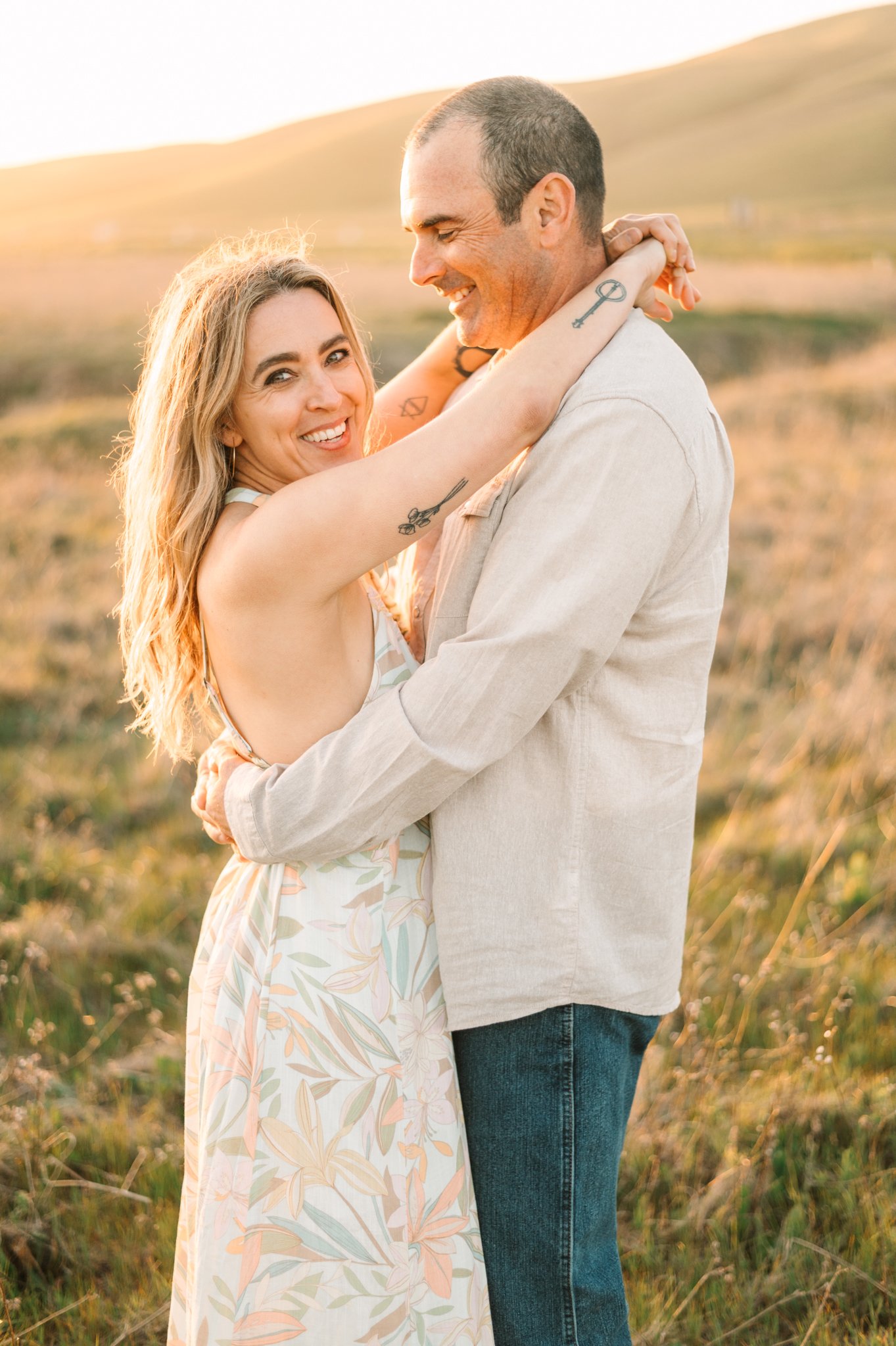 A happy couple embracing outdoors during sunset, with rolling hills in the background.