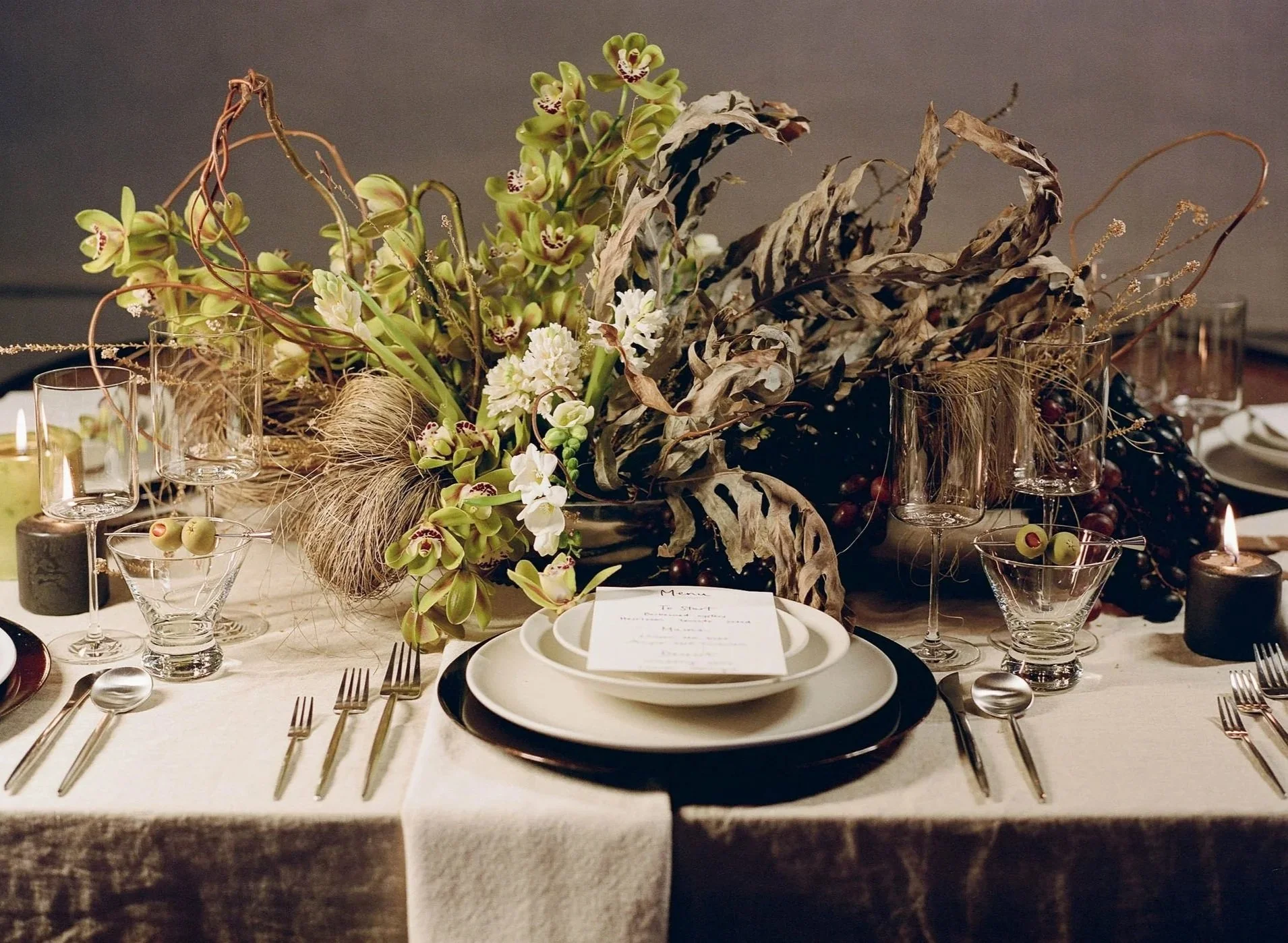 Elegant dining table with a floral centerpiece, candles, wine glasses, and place settings.