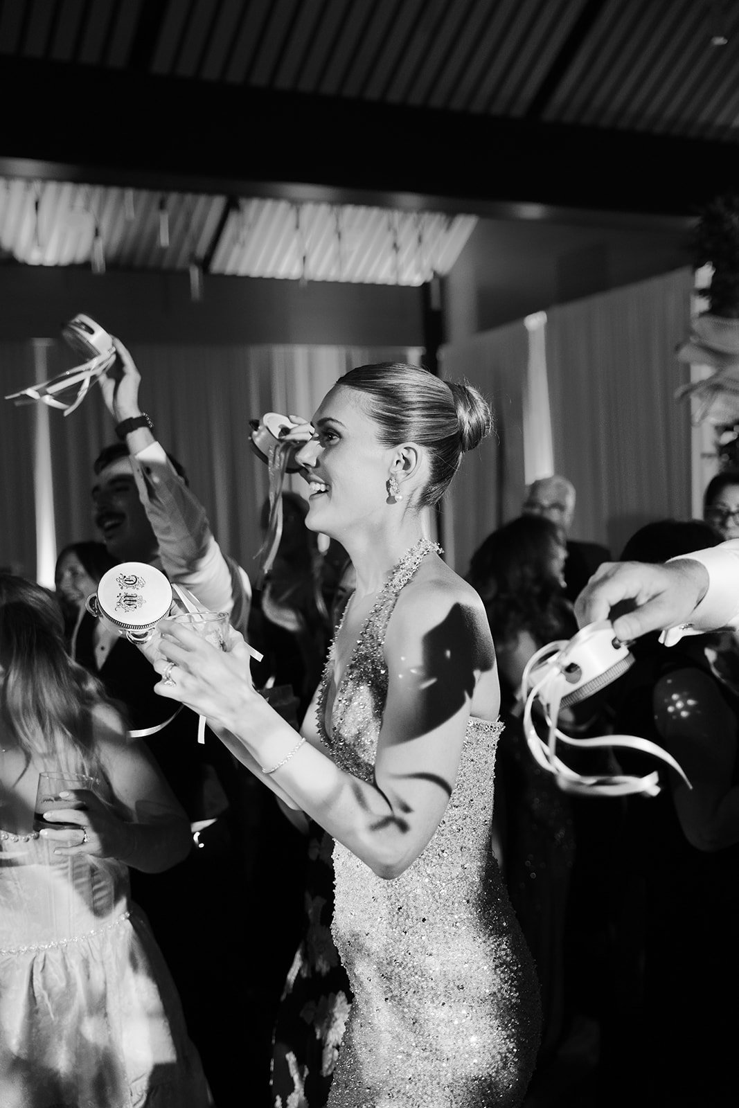 A woman in a sparkling dress celebrating at a party, holding a glass and surrounded by others with party accessories.