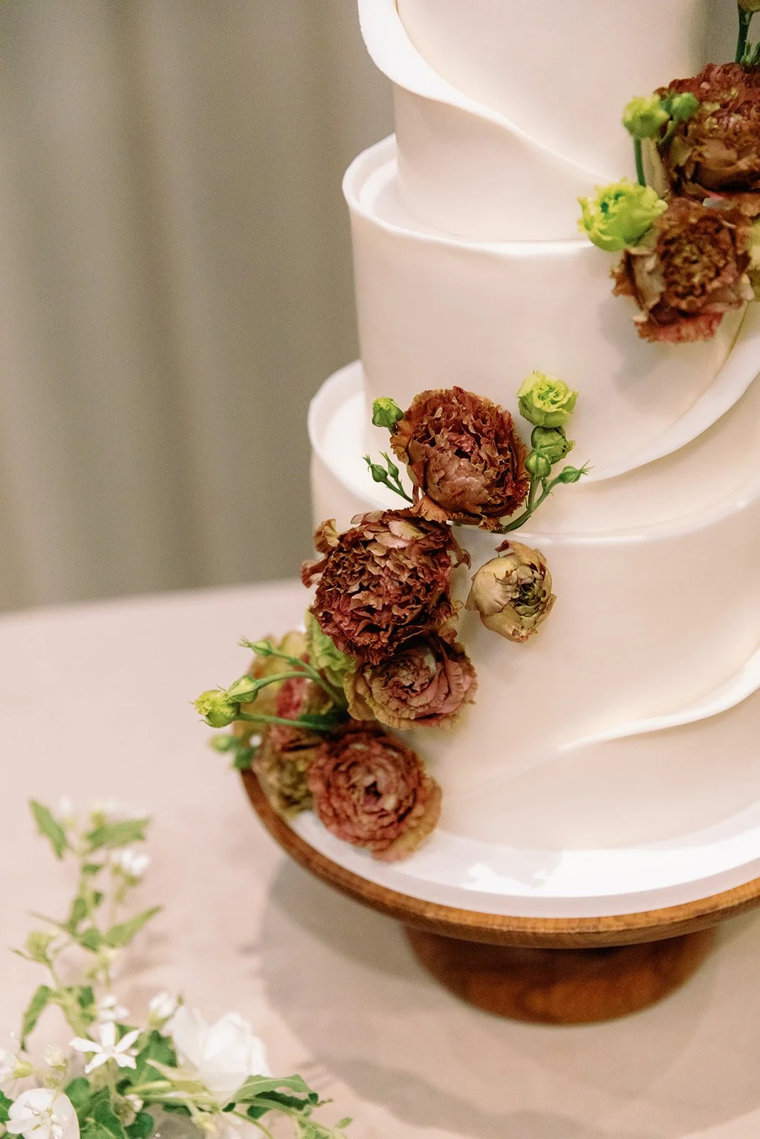 A multi-tiered wedding cake with white icing, decorated with dried flowers, on a wooden cake stand.