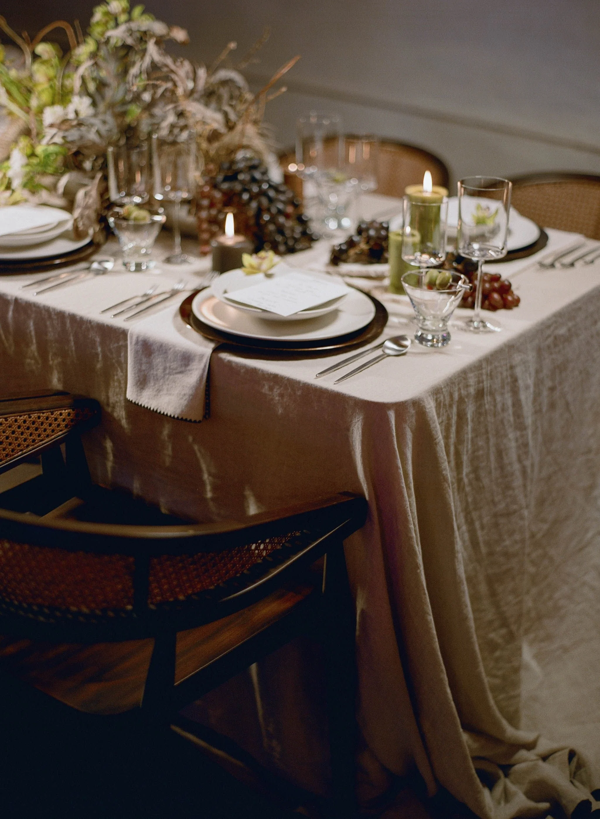 A decorated dining table set for a meal with plates, silverware, glasses, and candles, with a floral centerpiece and candles as decoration.