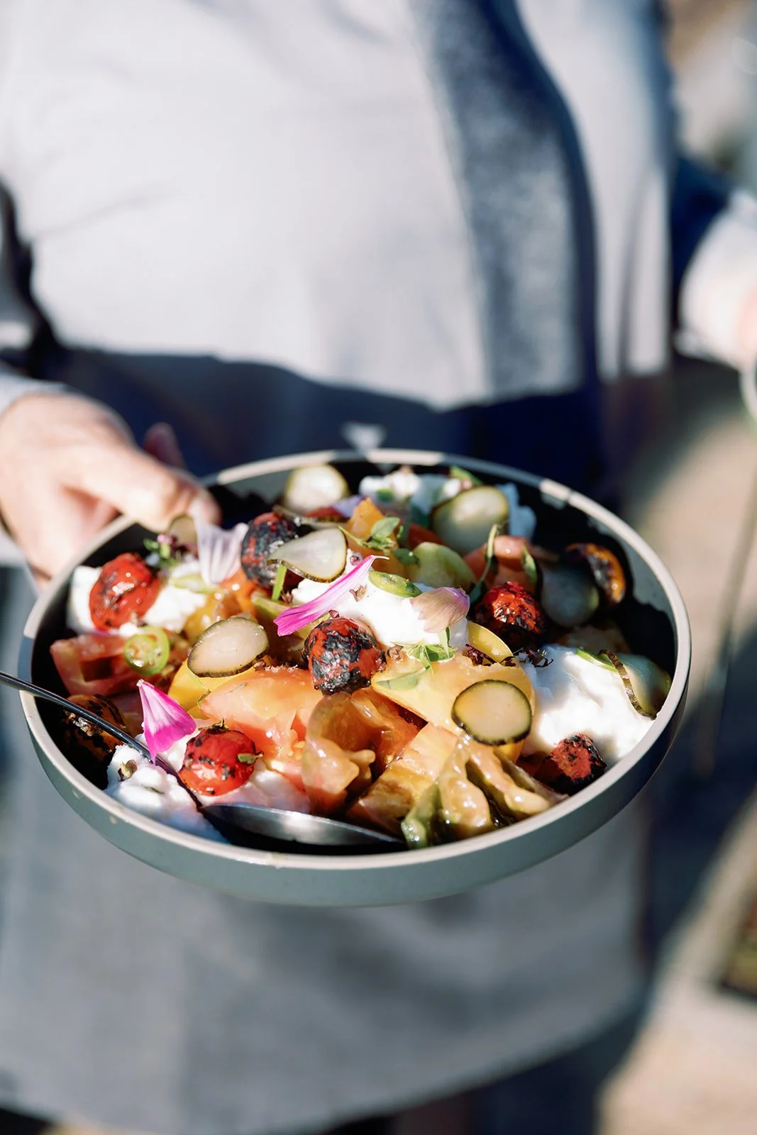 Person holding a bowl of colorful salad with various vegetables and garnishes.