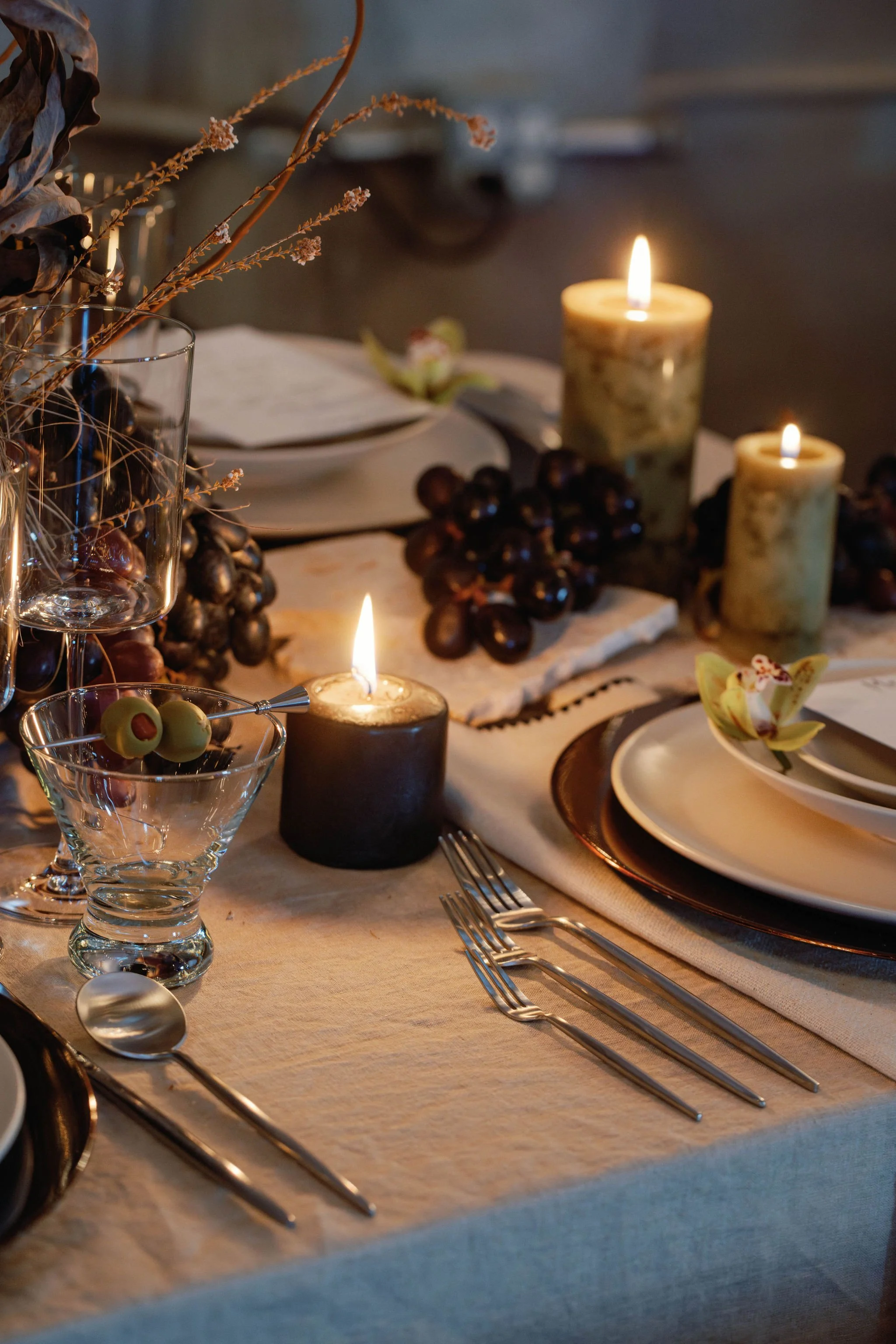 A elegantly set dinner table with lit candles, grapes, and decorative flowers, creating a warm and inviting atmosphere.