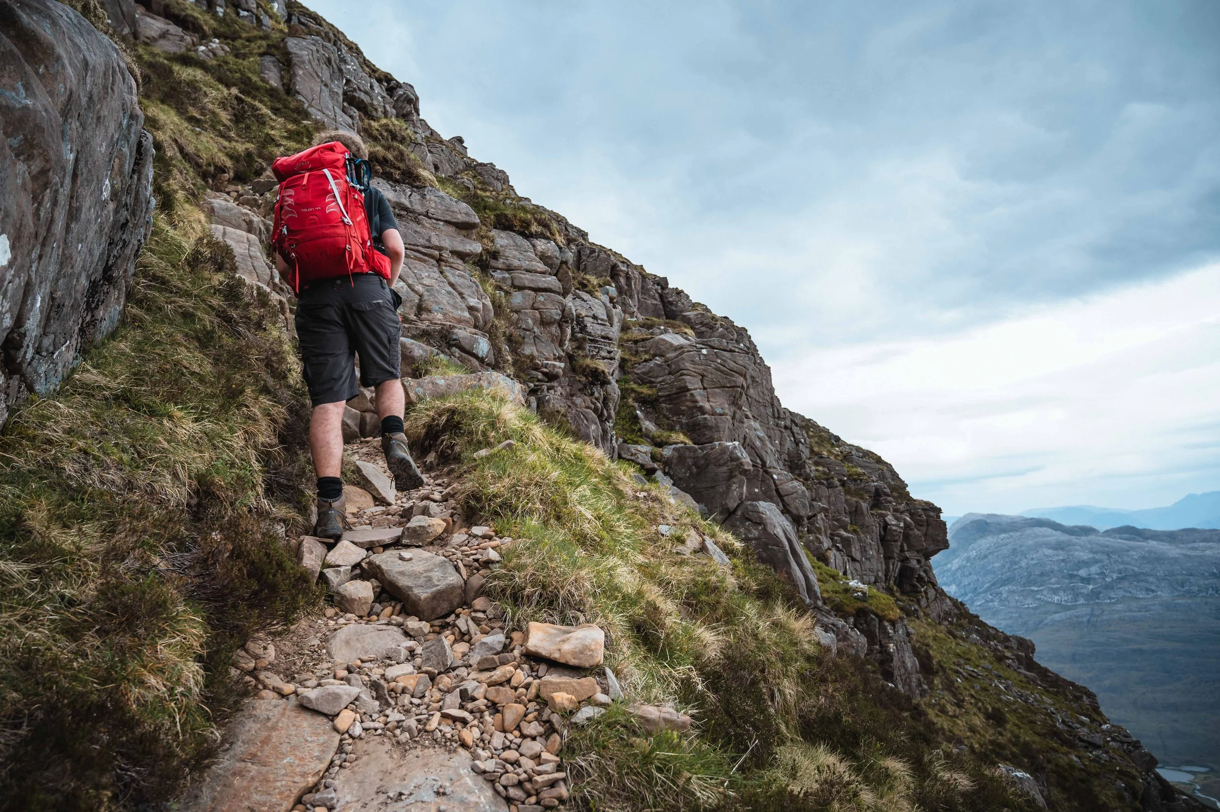 A man with a red rucksack climbs Liathach