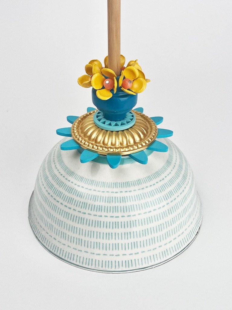 a detail of the "sky" sculpture, focusing on its base- a blue and white ceramic bowl, topped with a golden flower and 5 miniature yellow flower sculptures