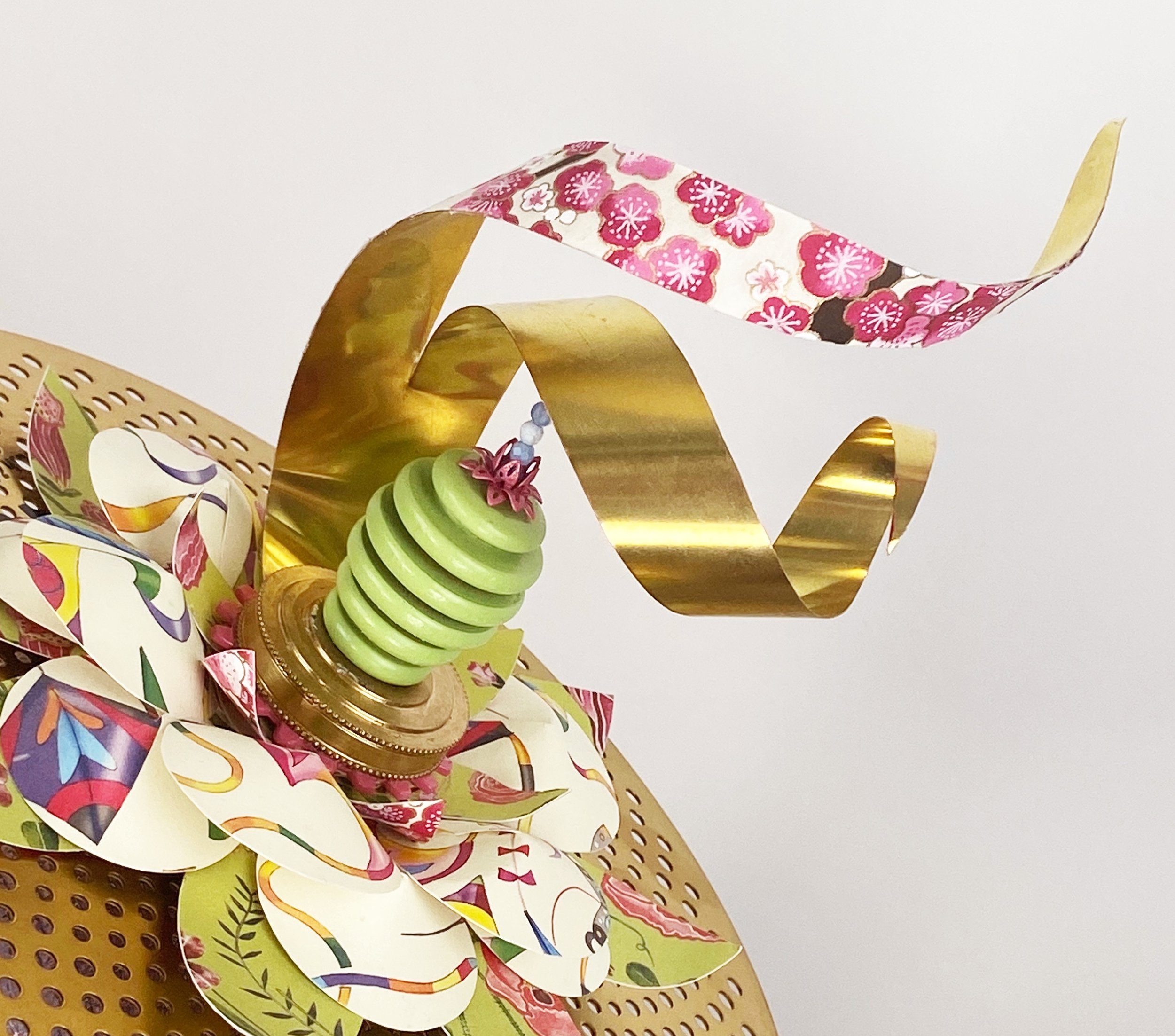 A detailed view of the top of the hat in the "hat" sculpture. Wavy metal ribbons fly out of a floral sculpture piece.