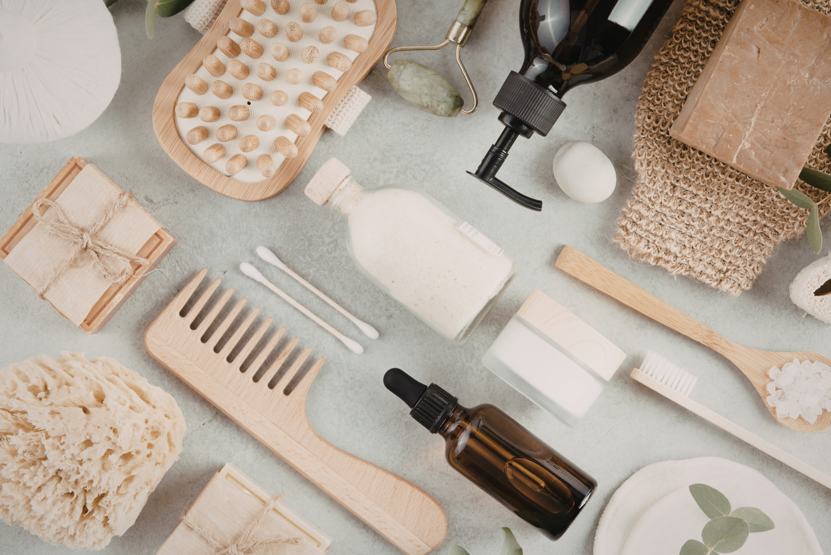 Flat lay of natural, non-toxic personal care items including wooden comb, body brush, reusable toothbrush, glass bottles, bar soap, and cotton accessories on a light background, representing a clean hormone-safe bathroom routine.