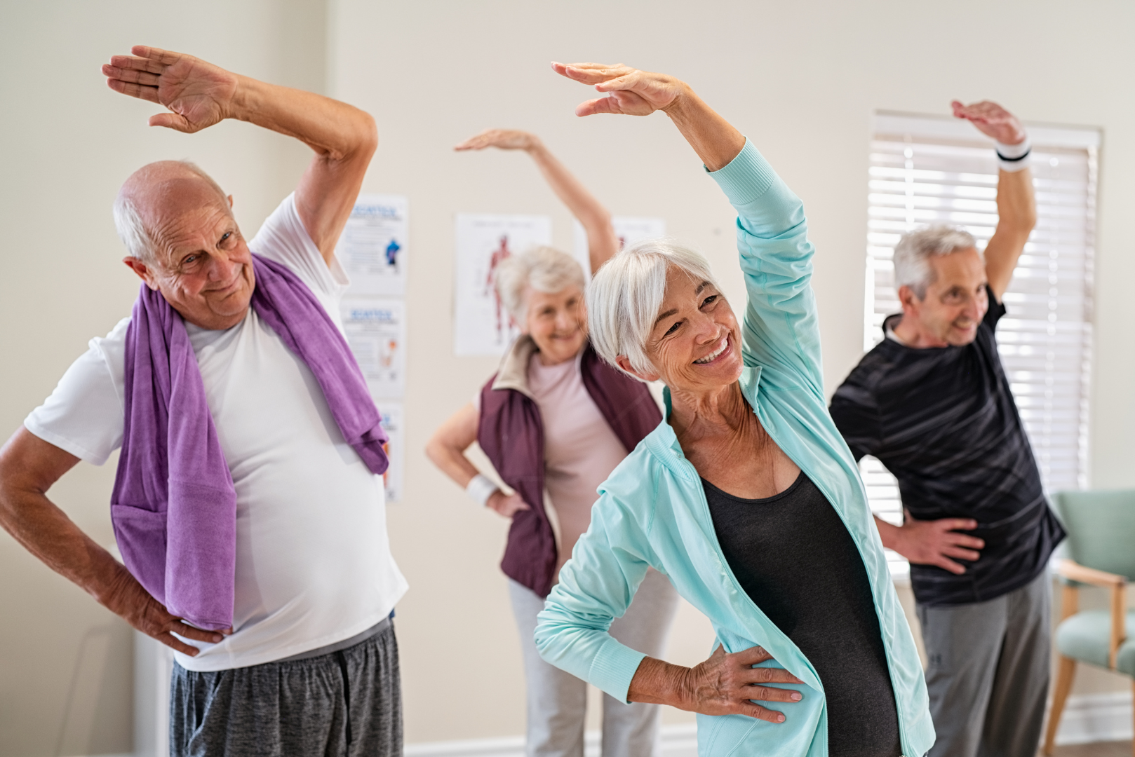 Group of active older adults in a fitness class doing side stretch exercises and smiling, demonstrating healthy mobility and movement as they age.