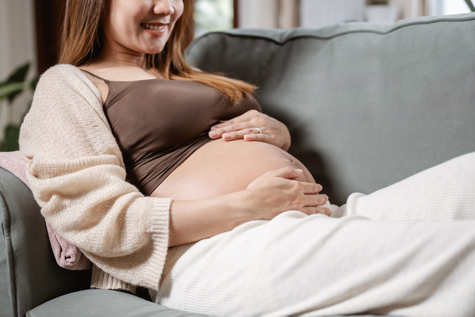 Pregnant woman relaxing on a sofa, smiling and gently holding her belly, representing a healthy pregnancy after strong fertility foundations.