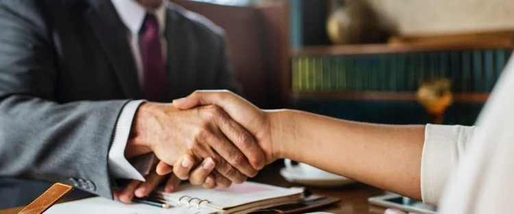 Close-up of two people shaking hands during a business meeting or interview in an office setting.