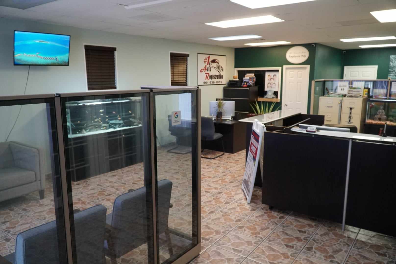 Interior of an office or reception area with a desk, chairs, glass display case, filing cabinets, a wall-mounted television, and framed pictures on the wall.