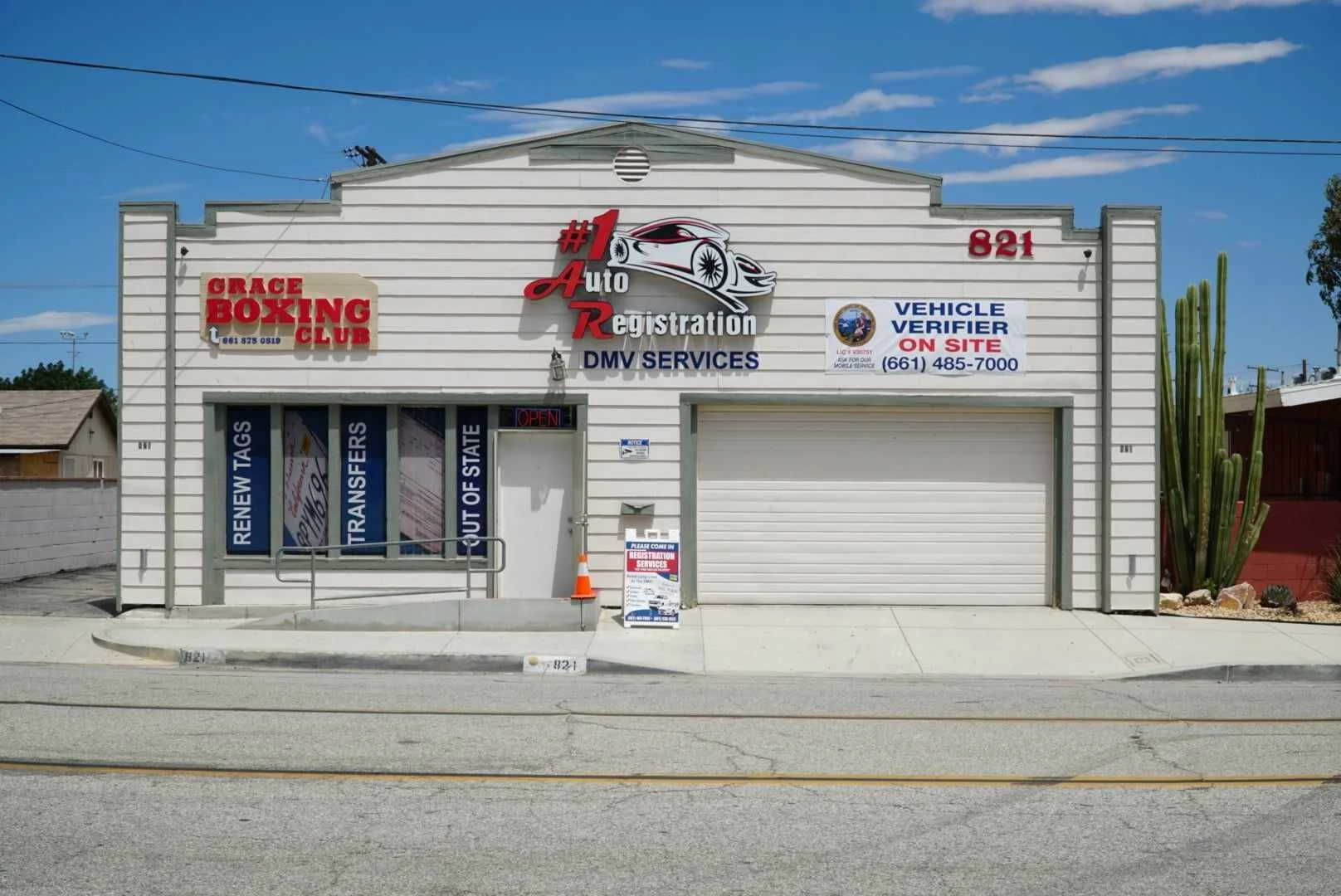 Exterior view of an auto registration business with signs for DMV services, a boxing club, and vehicle verification on site, located at 821 on a sunny day.