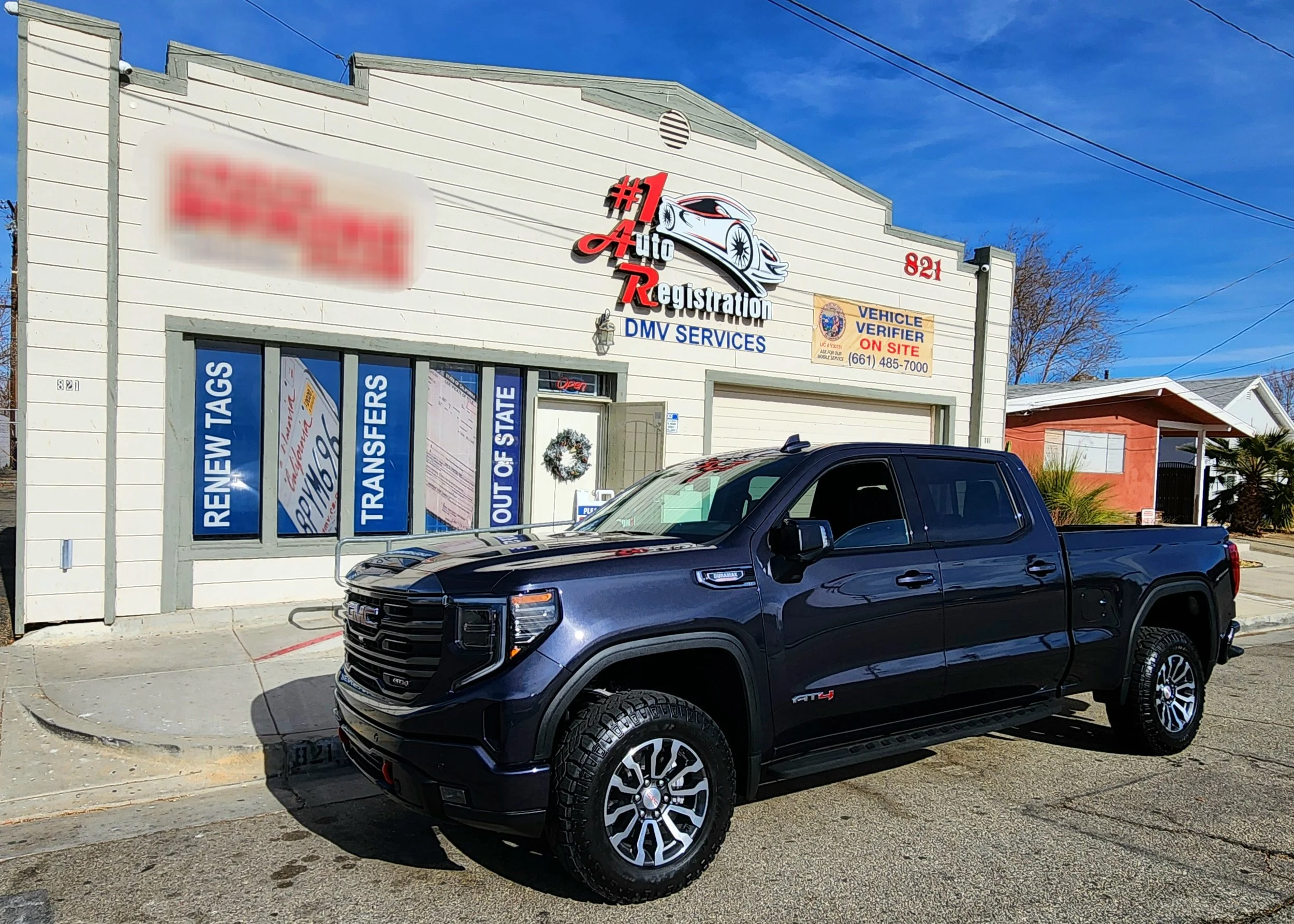 Blue pickup truck parked outside an auto registration and DMV services shop with a white building and blue sky.