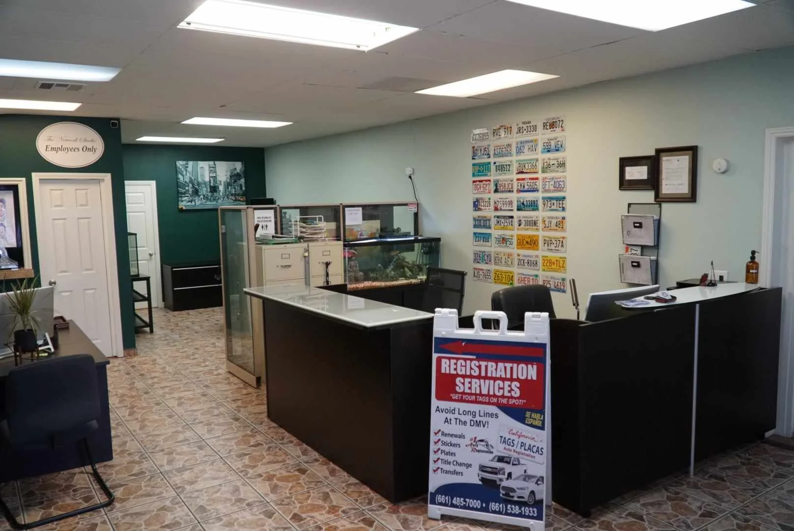 Office reception area with registration services sign, black desk, blue wall with license plates, small tank, and office furniture.