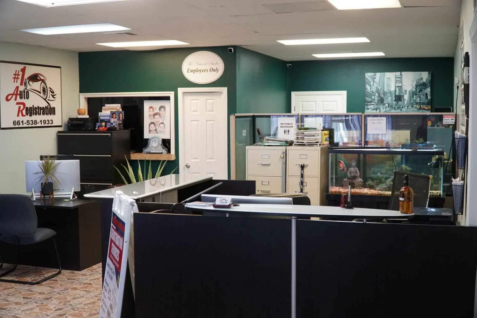 Reception area of an auto registration office with a sign that reads '#1 Auto Registration' and a phone number, a desk with a computer, a fish tank, filing cabinets, and various office supplies.