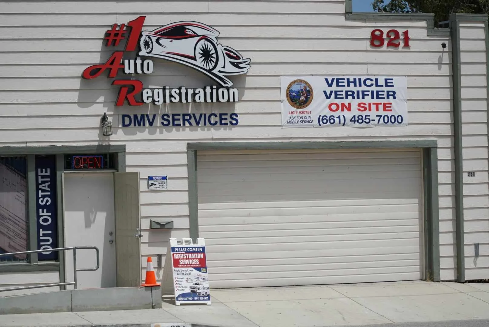 Front of an auto registration and DMV service shop with signs, including a large logo with a car, and a banner indicating vehicle verification on site. There is an