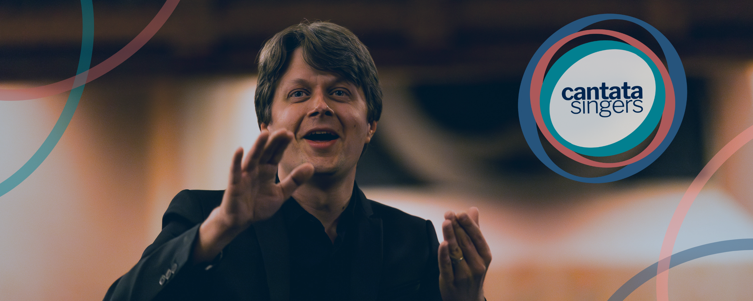 A smiling man uses his hands in open and inviting gestures to conduct a chorus in joyful song.