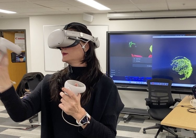 Fine Artist Robbi Firestone explaining the infinite usages of virtual reality for bettering education by creating an artwork projected behind her at the Community College of New Mexico CNM Advanced Technology Center Film school.