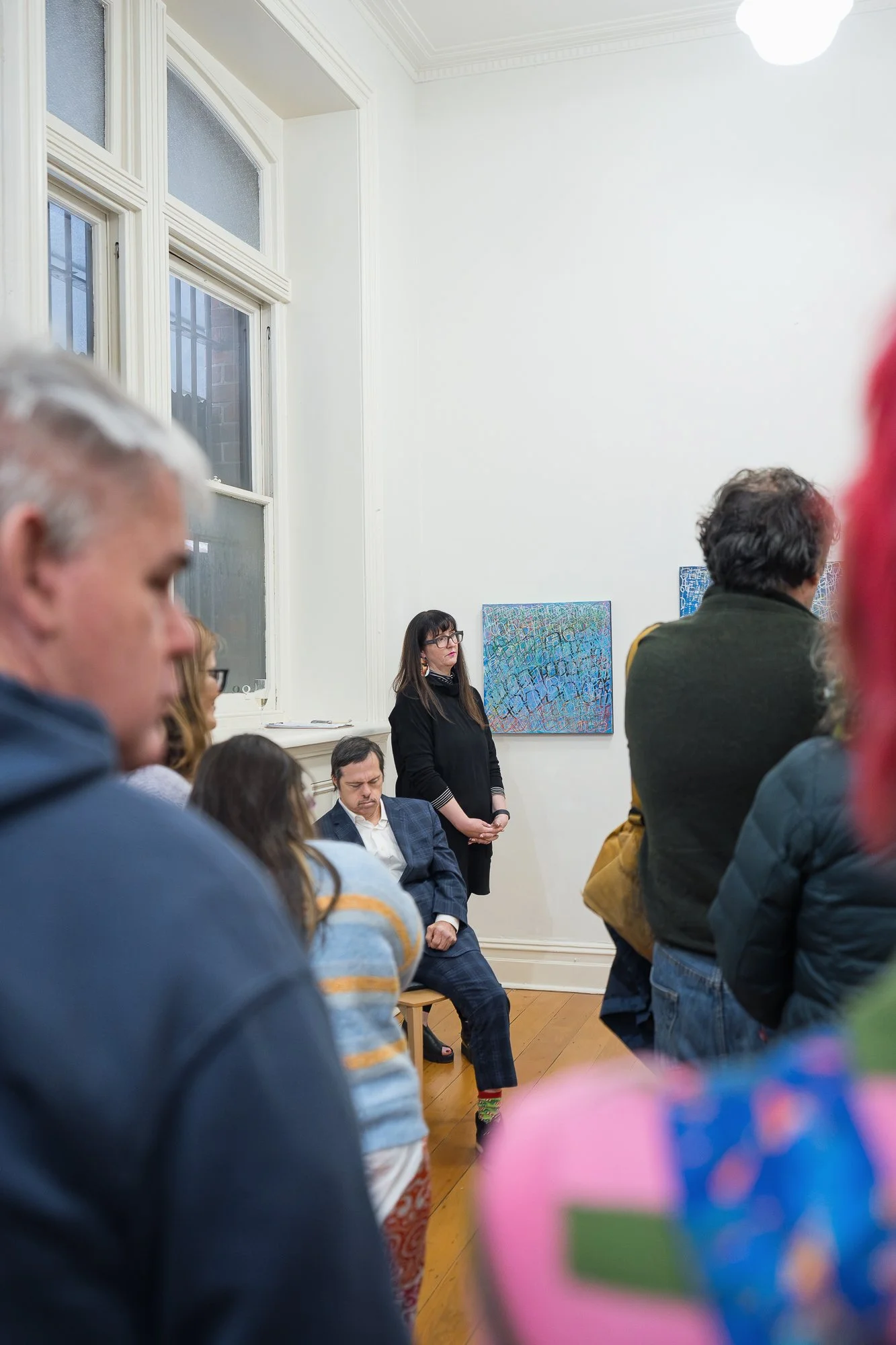 The welcome address in progress — a woman stands at the front of a packed room of guests, all eyes forward.