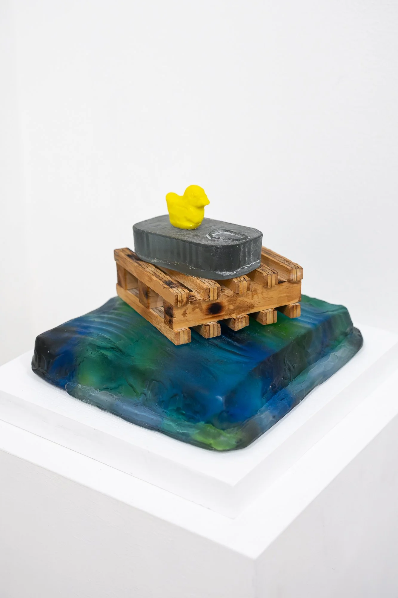 Close up of a small glass and wood sculpture on a white plinth
