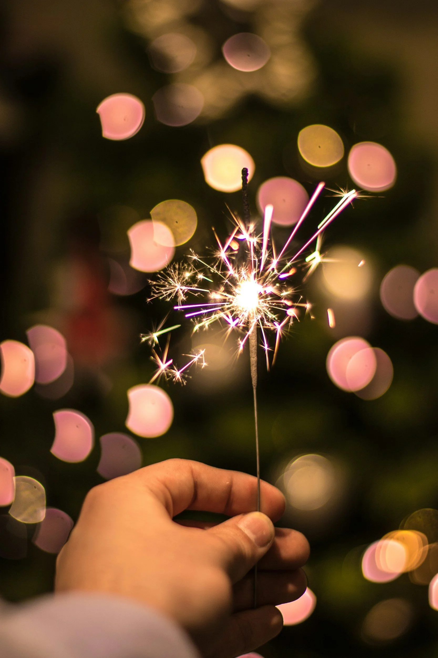 Hand holding a lit sparkler with blurred bokeh lights in the background.