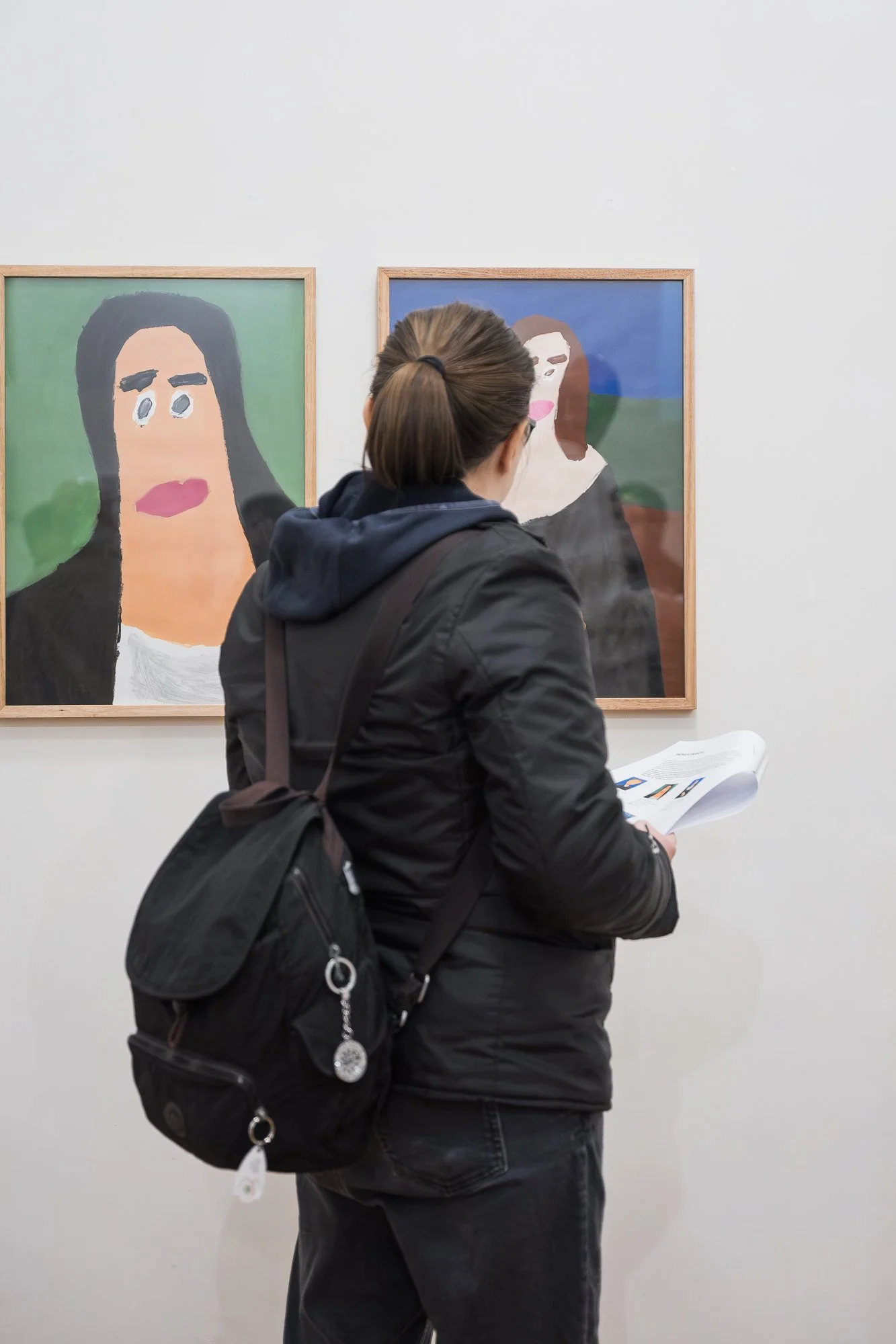 Woman viewed from behind reading an exhibition booklet in front of two portrait paintings.