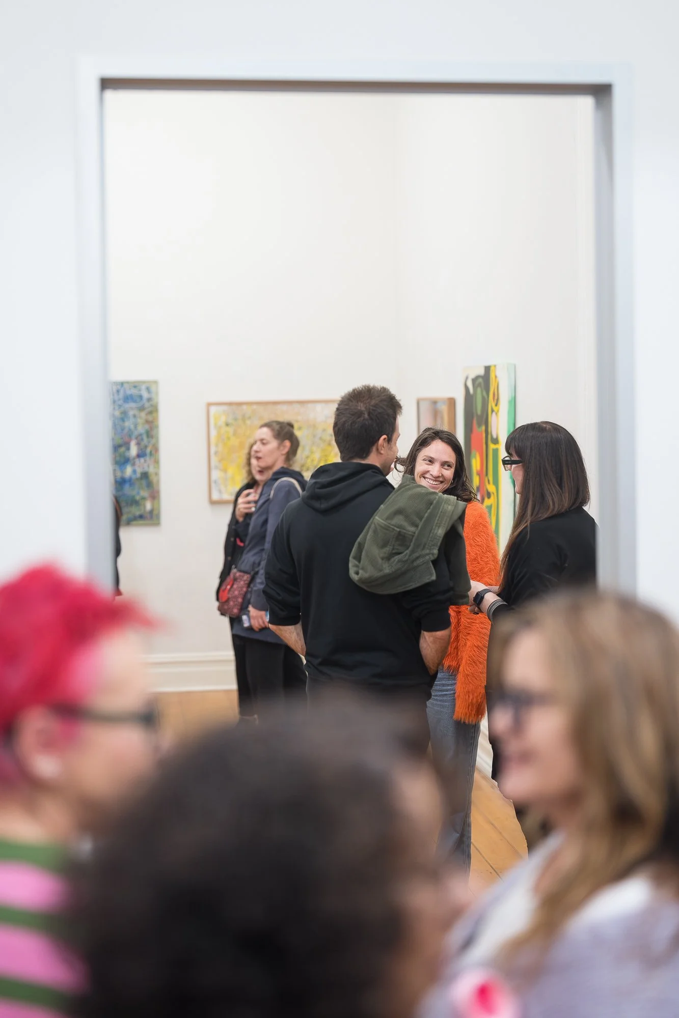 A smiling woman looks back through a crowd of guests as people chat across two connected gallery spaces.