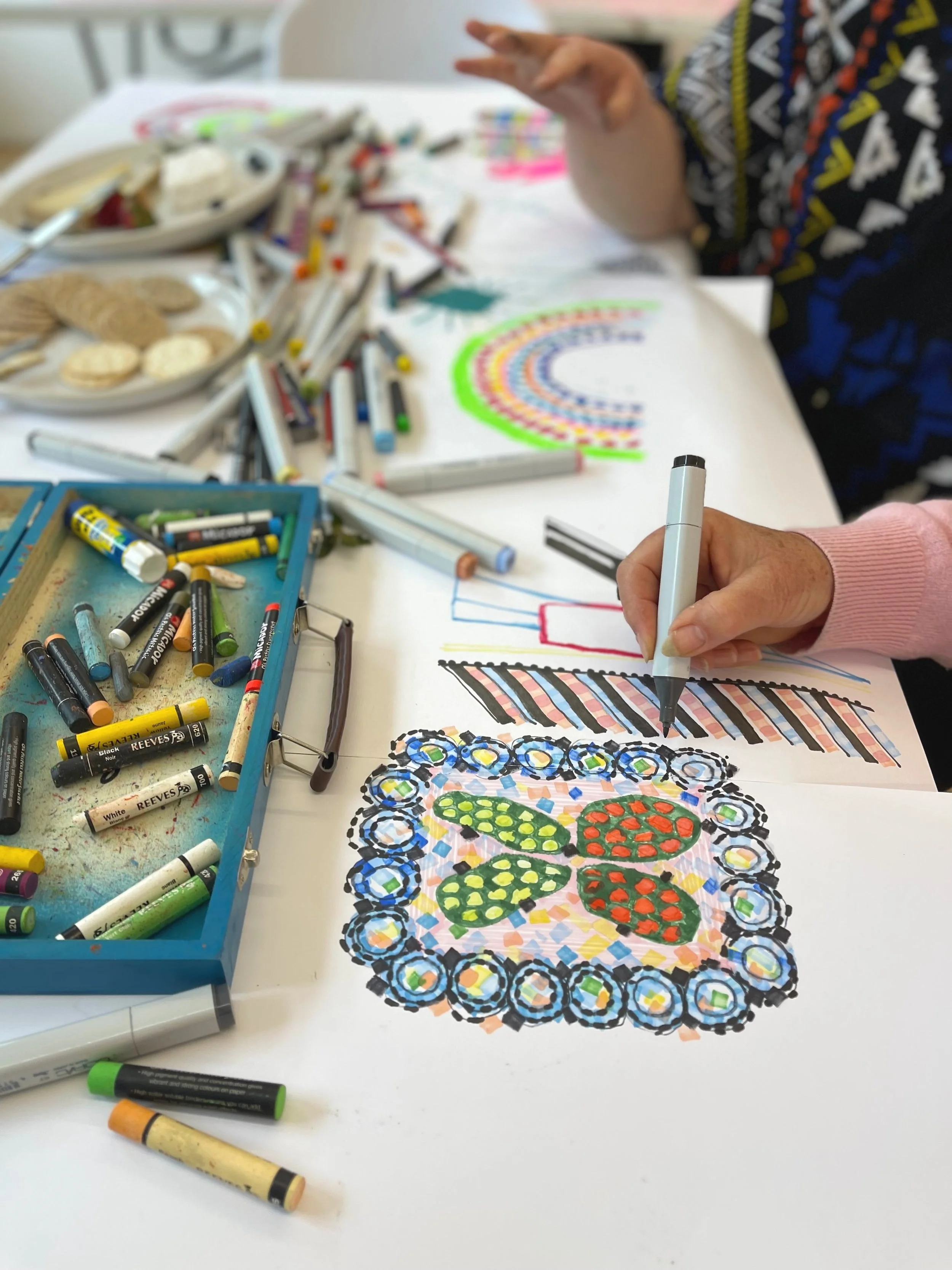 Close up view of an artist's hand making a brightly coloured piece of artwork.