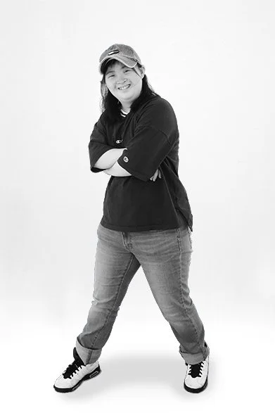 Person wearing a hat, casual shirt, jeans, and sneakers standing with arms crossed.