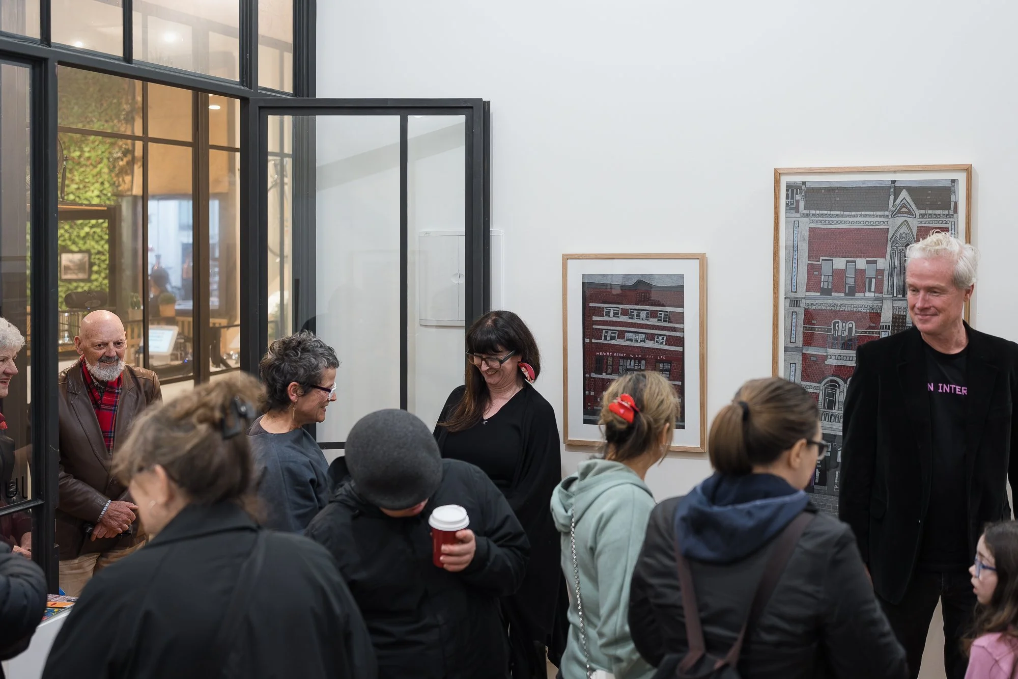 Group of visitors gathered near a glass-paned internal doorway, framed building illustrations on the wall behind them.