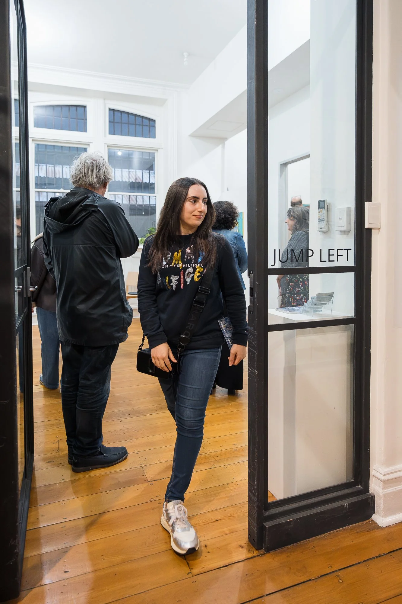 A visitor steps through the Jump Left entrance doors, the gallery humming with activity behind her.