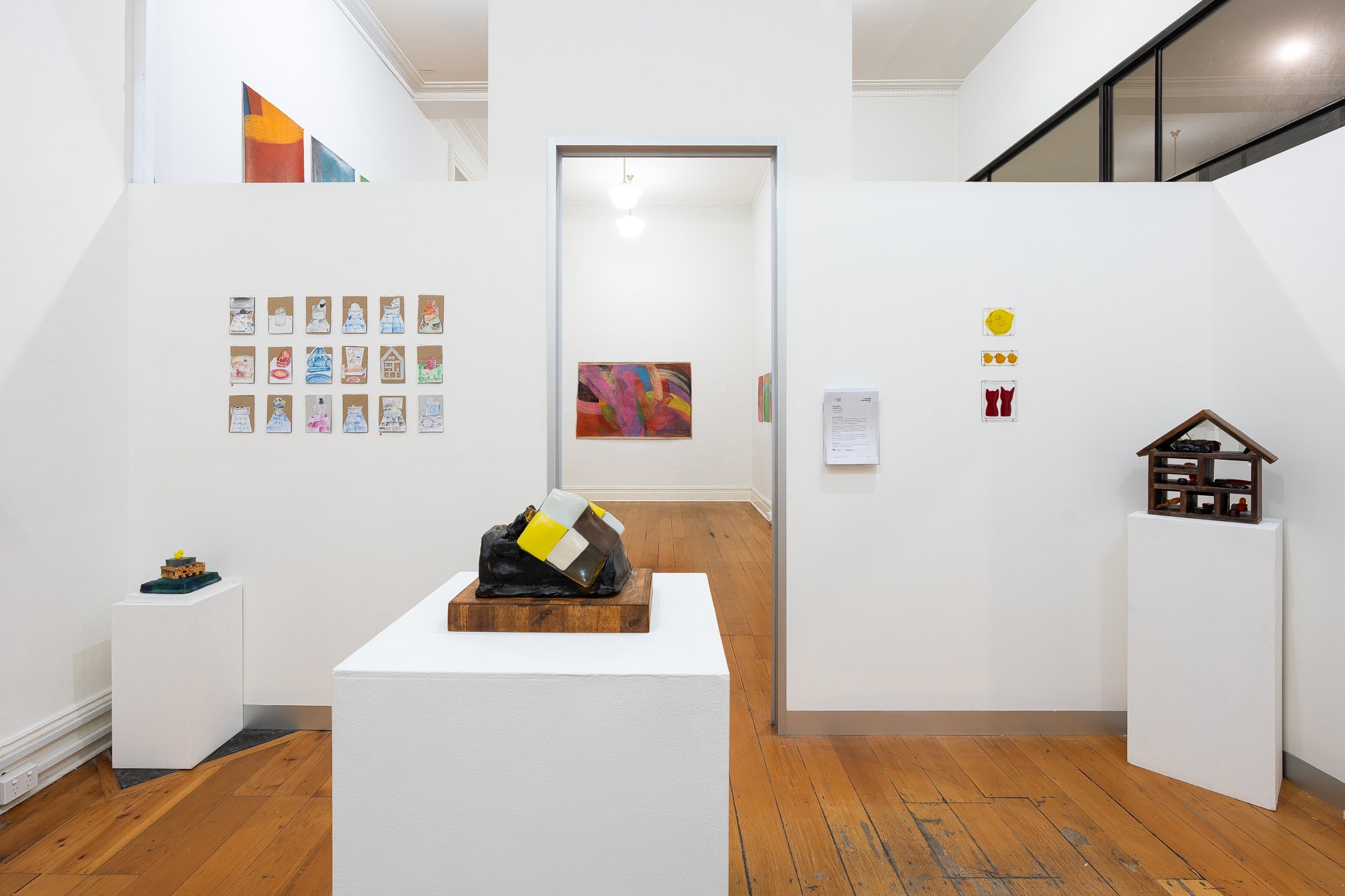 Installation image of mixed media artworks in a white gallery space with wooden floors