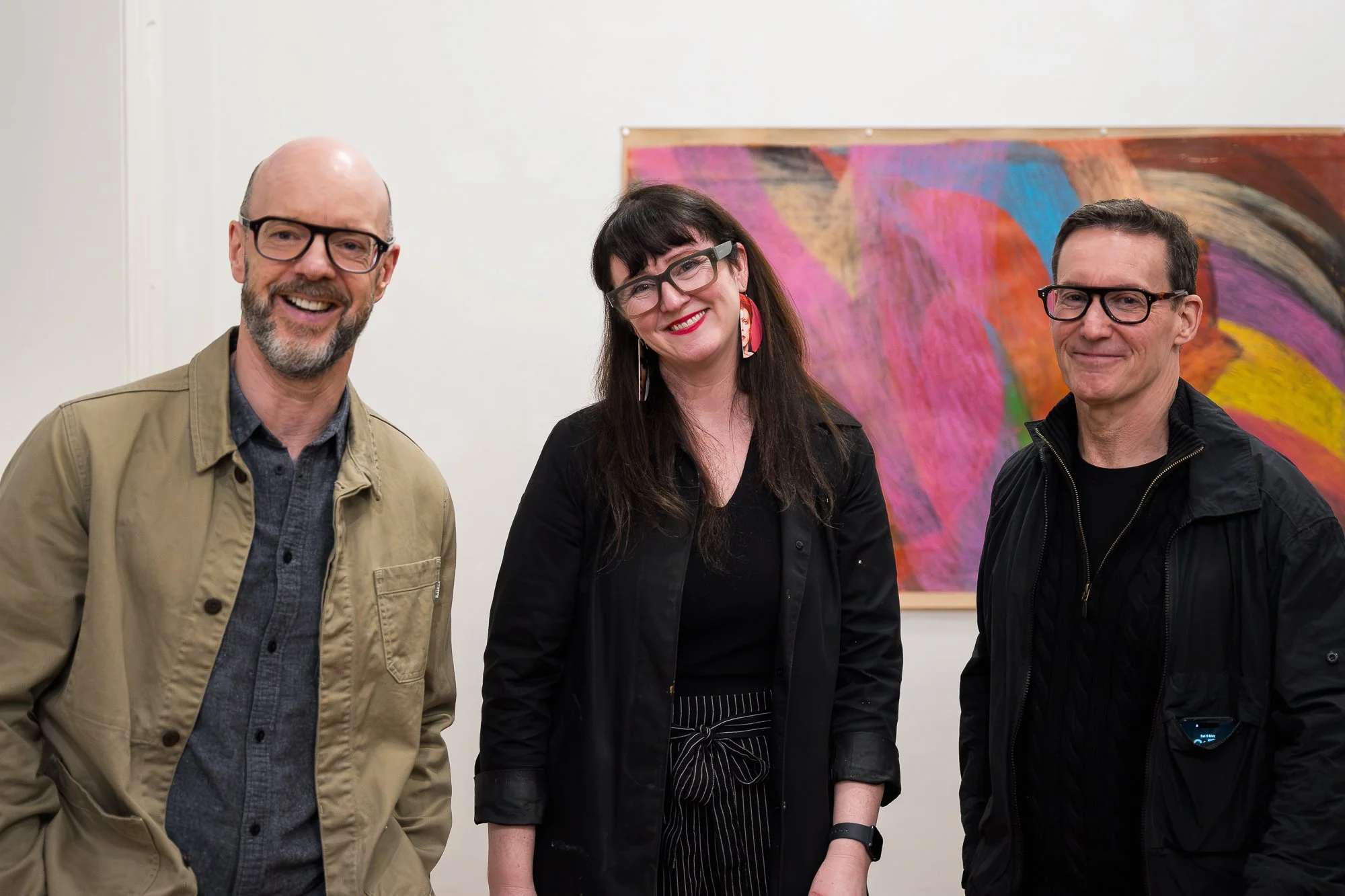 Three people looking at the camera, happy and enjoying themselves with a colourful artwork in the background