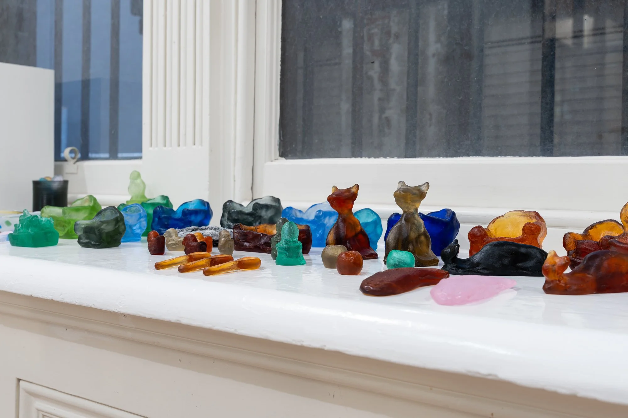 Installation of small colourful glass artworks on a white shelf