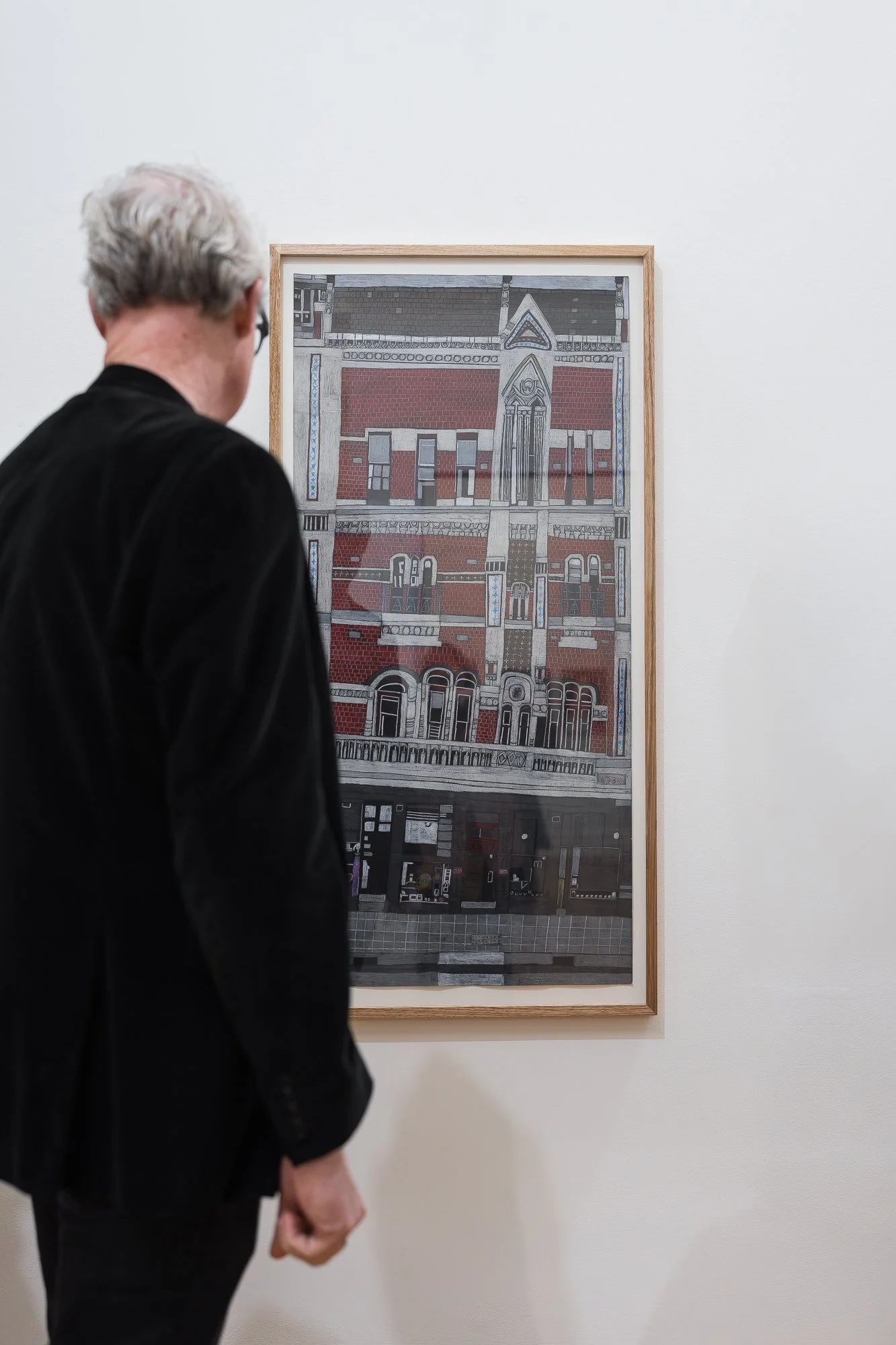 Man viewed from behind looking at a tall framed illustration of a red-brick heritage building facade.