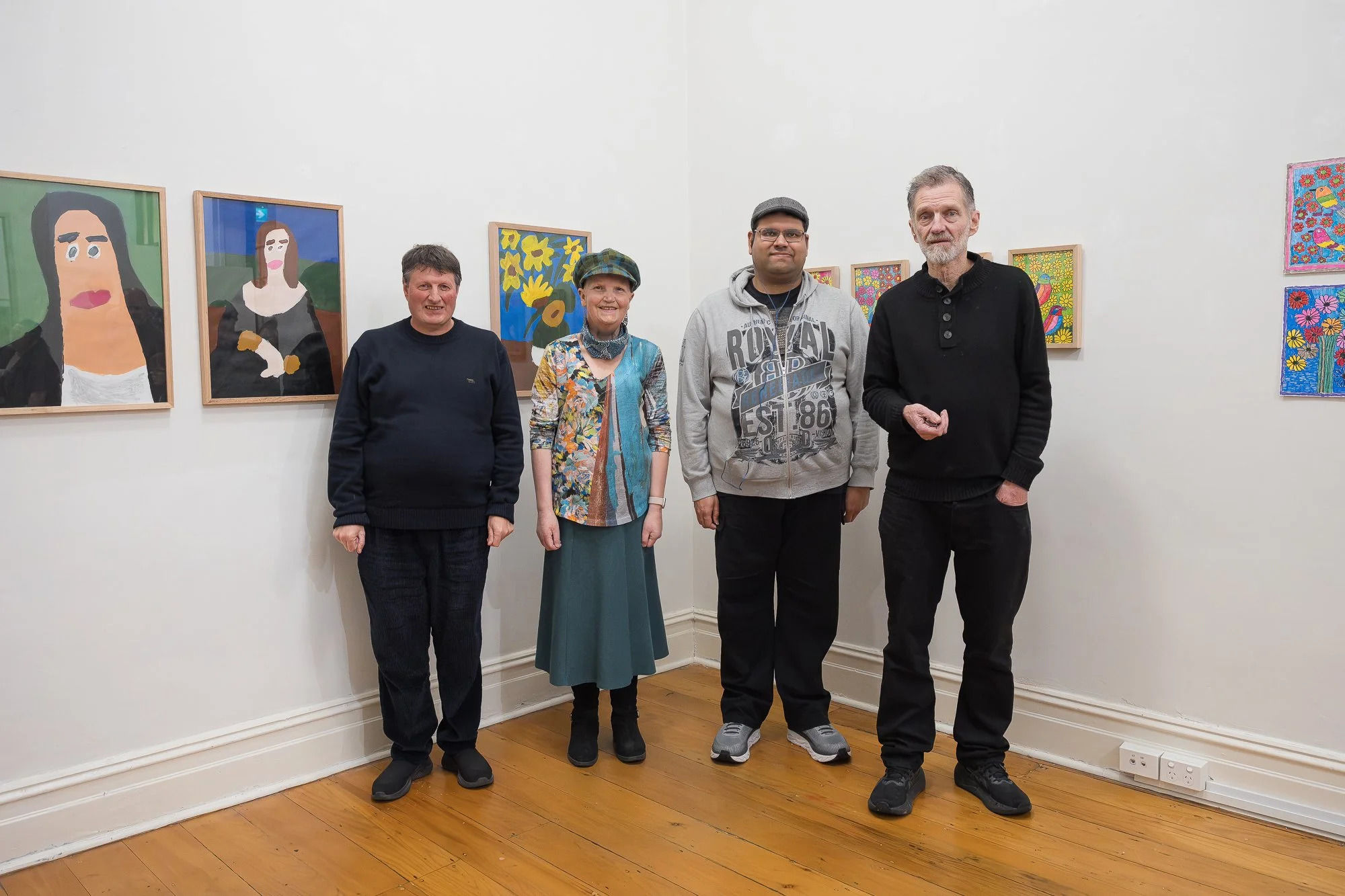Group of  four people posed together for a photo in front of portrait and floral paintings (appears to include artists and staff).