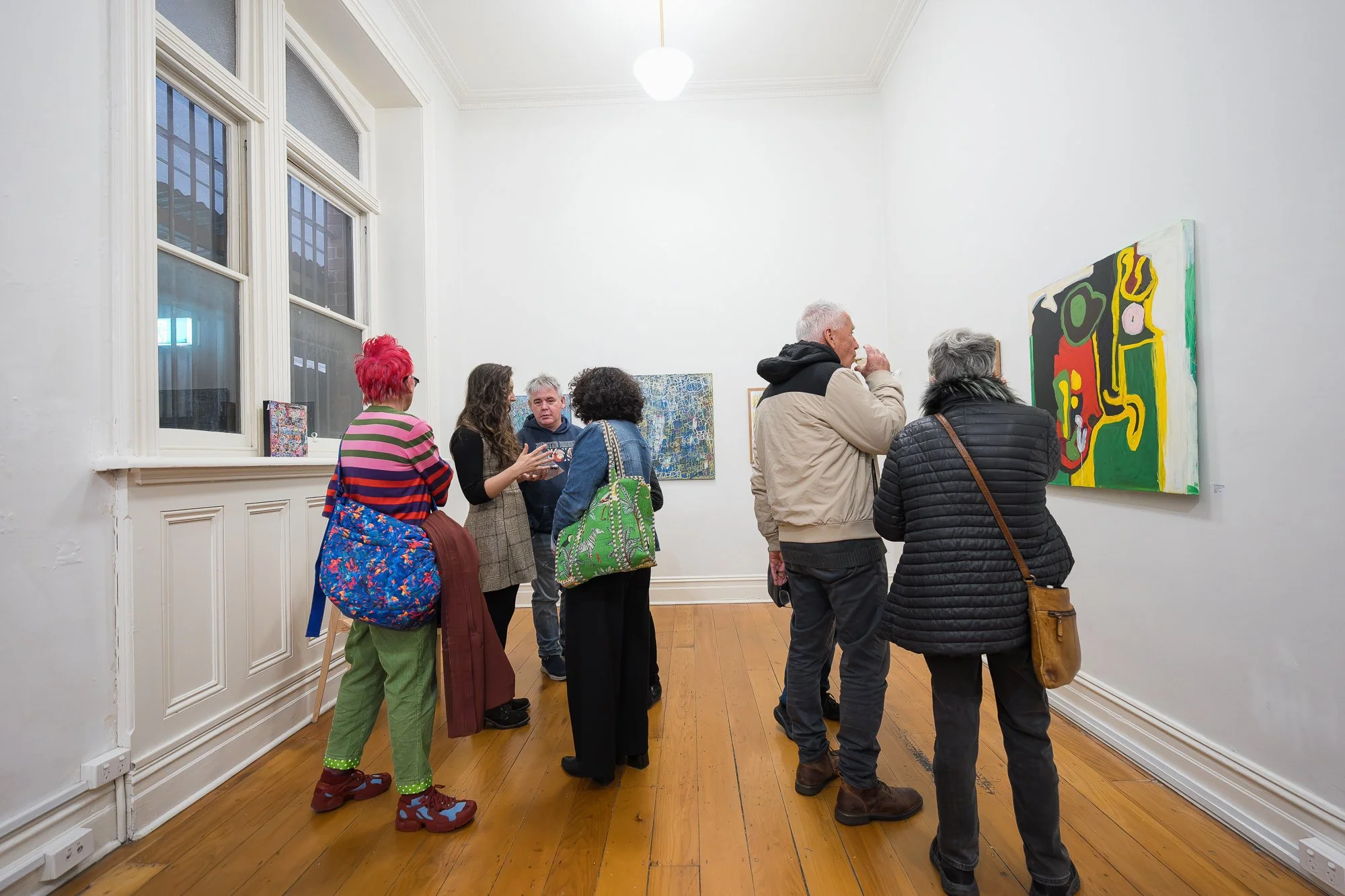 Guests mingle in a high-ceilinged gallery room, with bold abstract paintings filling the walls around them.