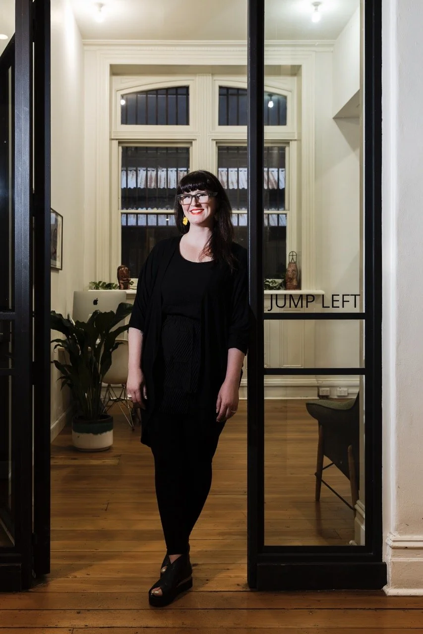Woman standing in office doorway with plants and "Jump Left" sign visible.
