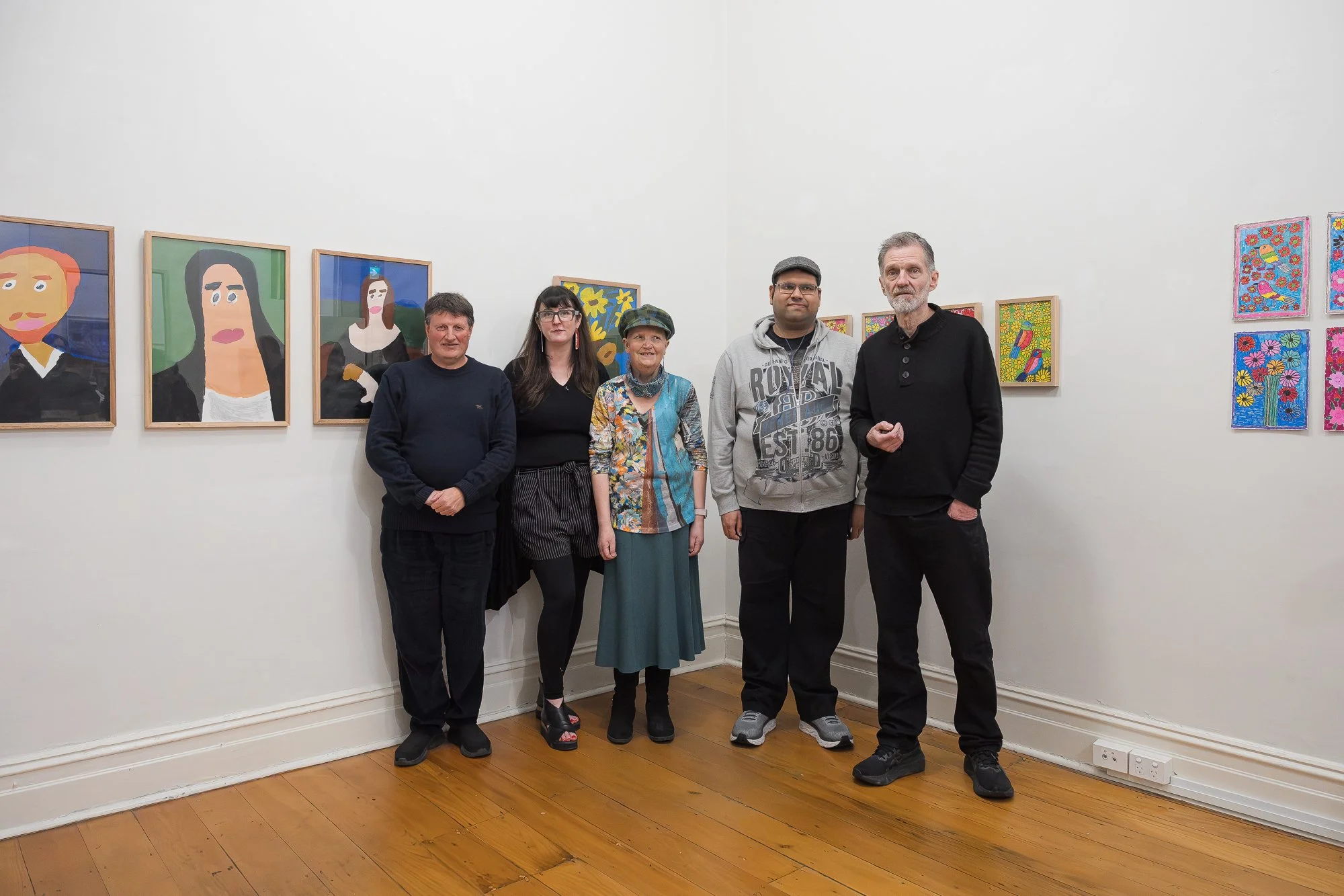 Group of five people posed together for a photo in front of portrait and floral paintings (appears to include artists and staff).
