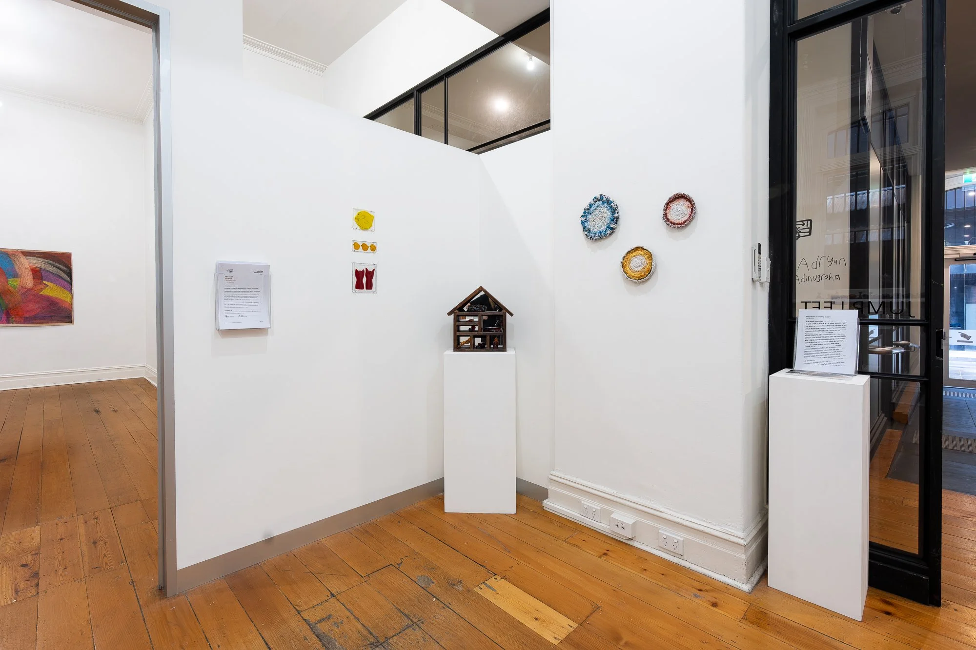 Installation image of mixed media artworks in a white gallery space with wooden floors
