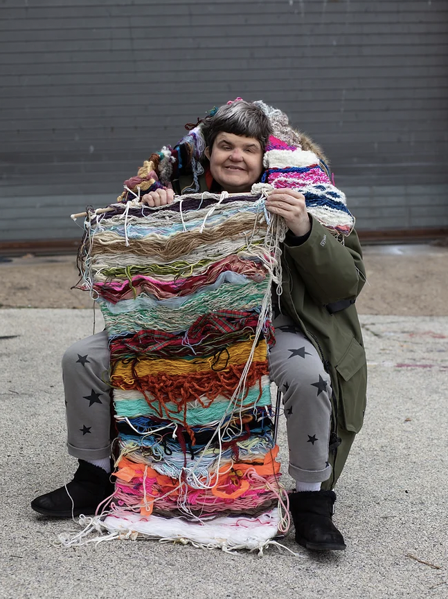 Person sitting and holding a large, colorful woven textile.