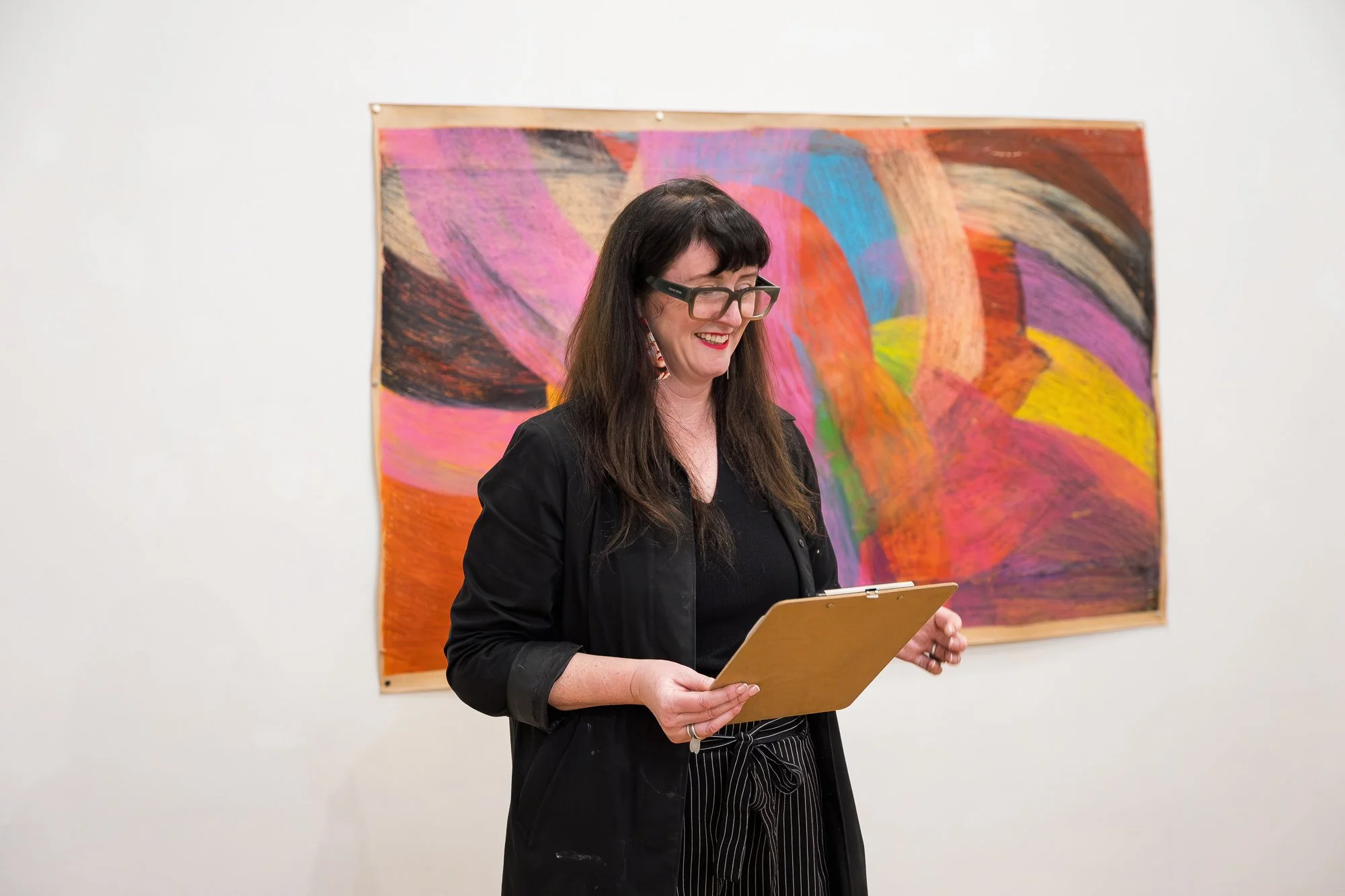 Woman reading from a clipboard in front of a large abstract drawing