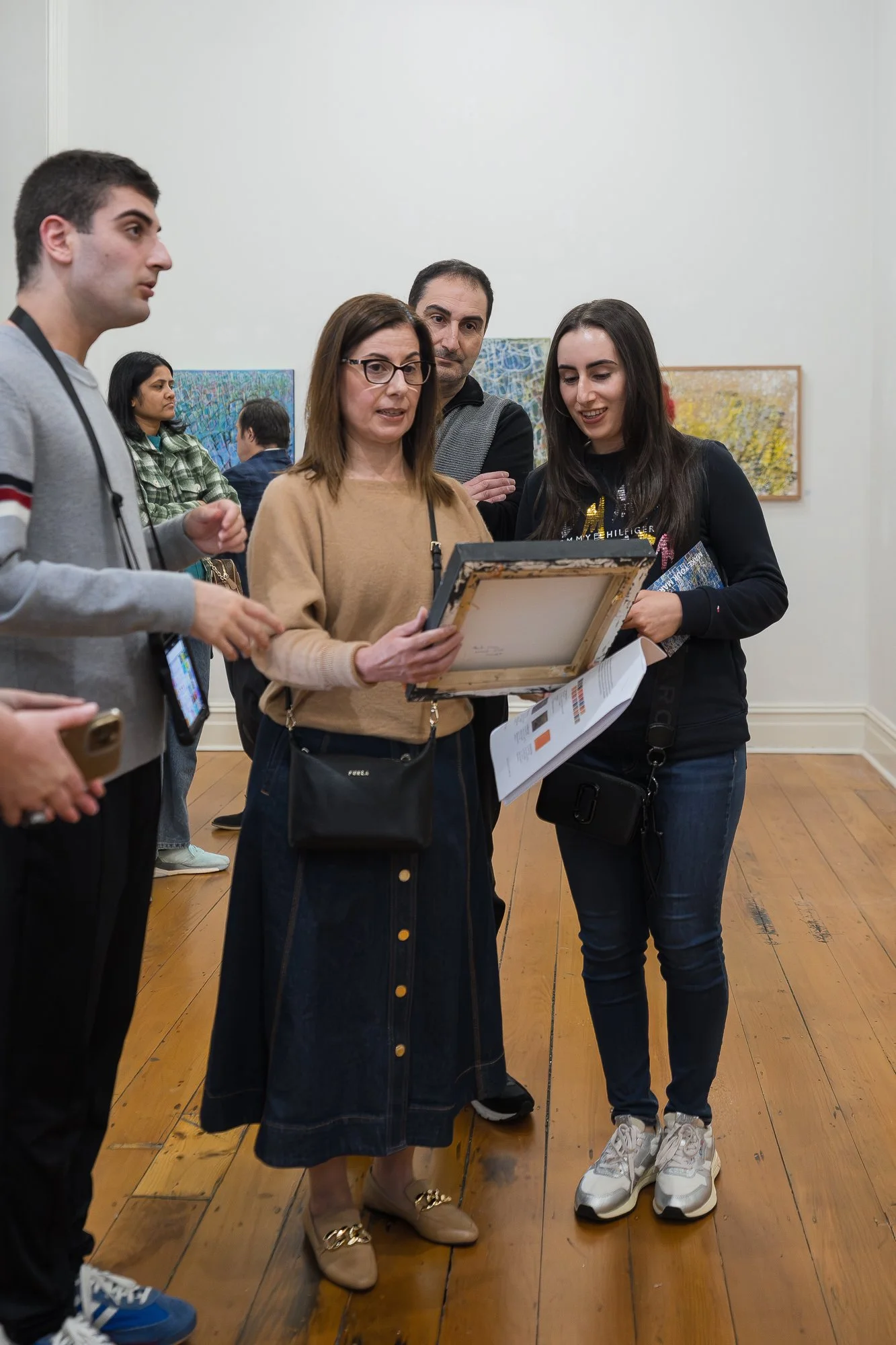 A family group huddles together, examining the back of a framed work.