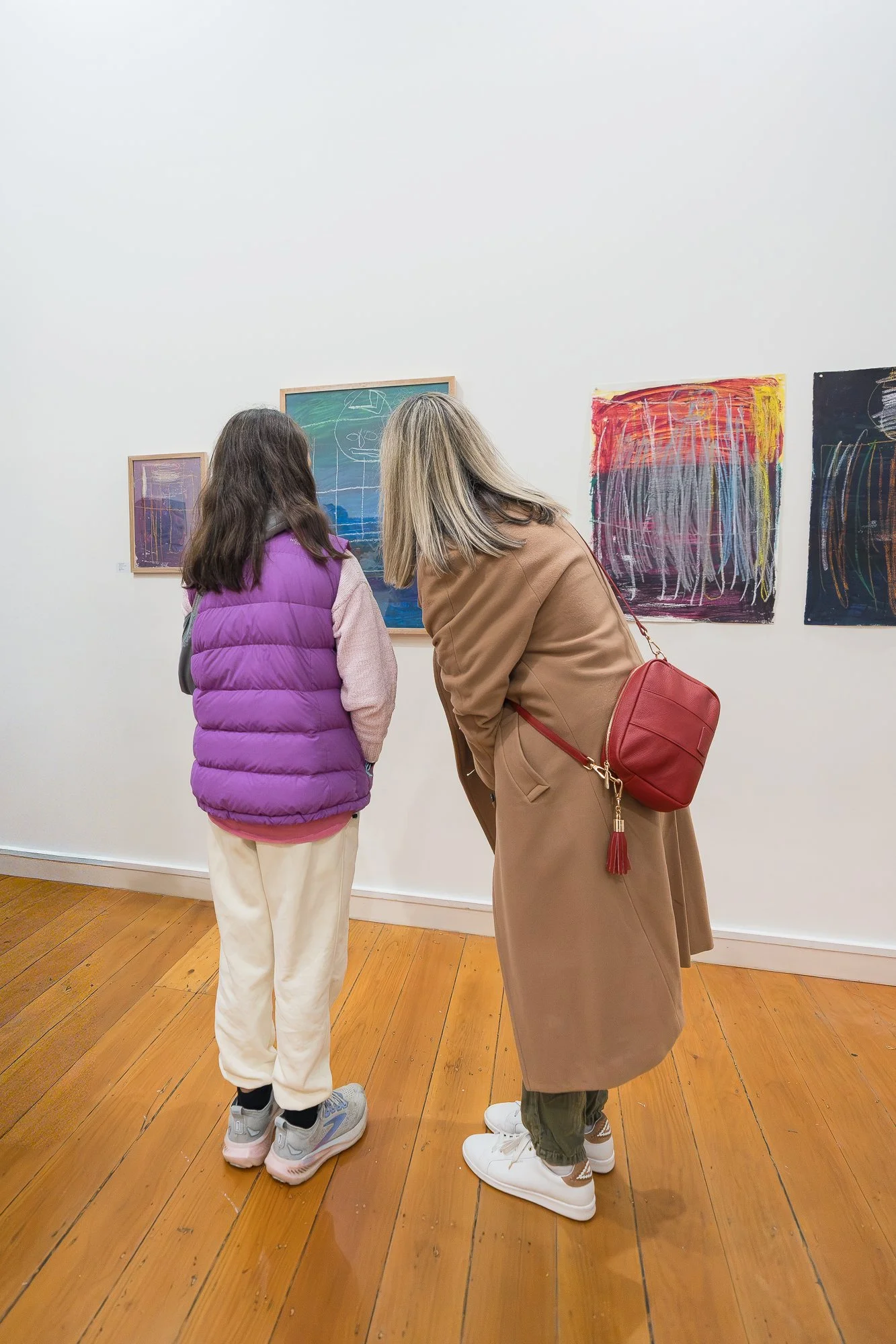 Two visitors lean in to look closely at works on the gallery wall.