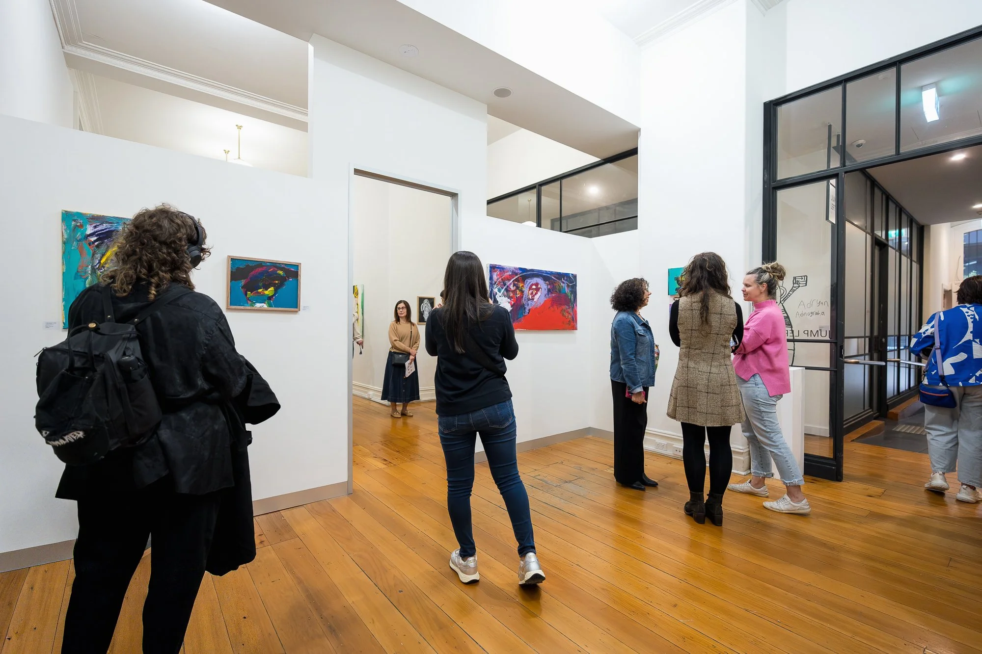 Visitors explore the main gallery space, with large expressive paintings visible across multiple walls and rooms.